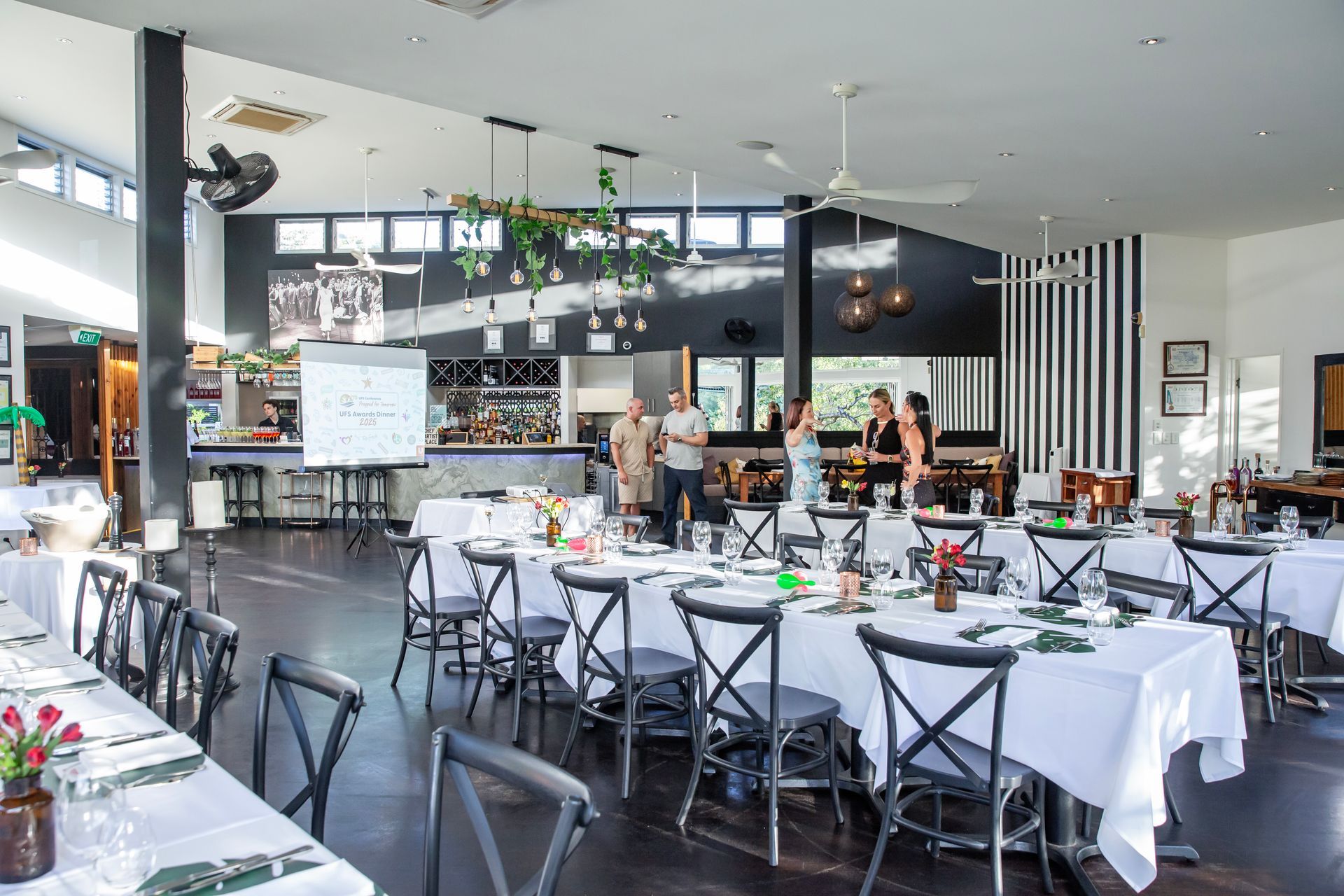 Conference set for a gathering, with tables covered in white cloths, bar in the background. Photography by Andy Williams