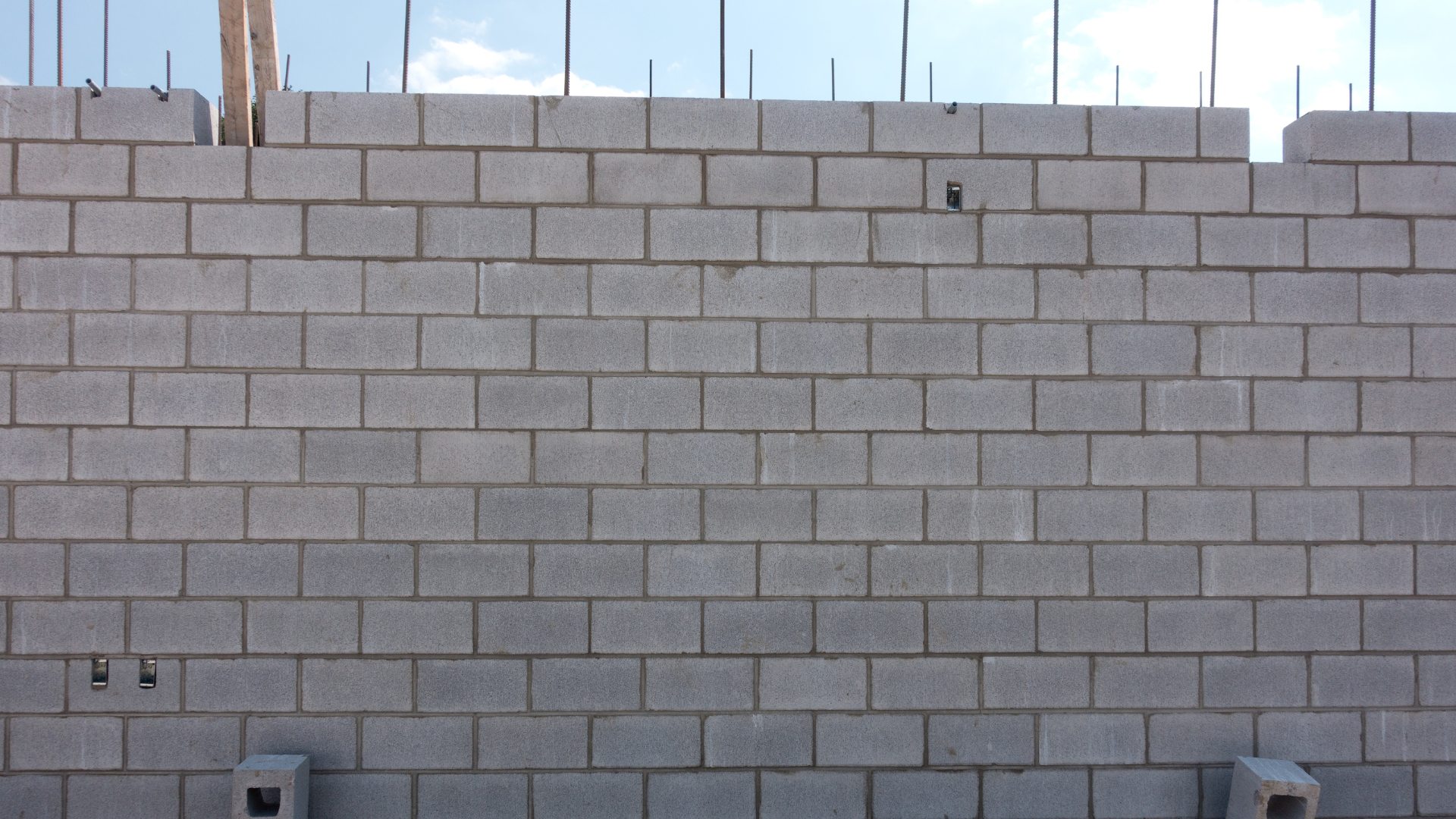 Concrete block wall under construction, with exposed rebar and wooden supports.