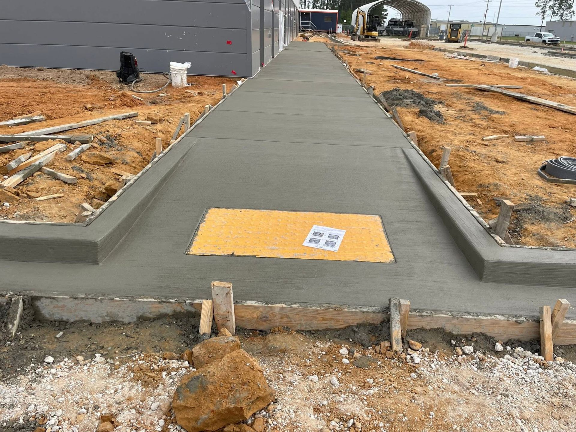 New concrete sidewalk at a construction site, with a yellow tactile pad in the center.