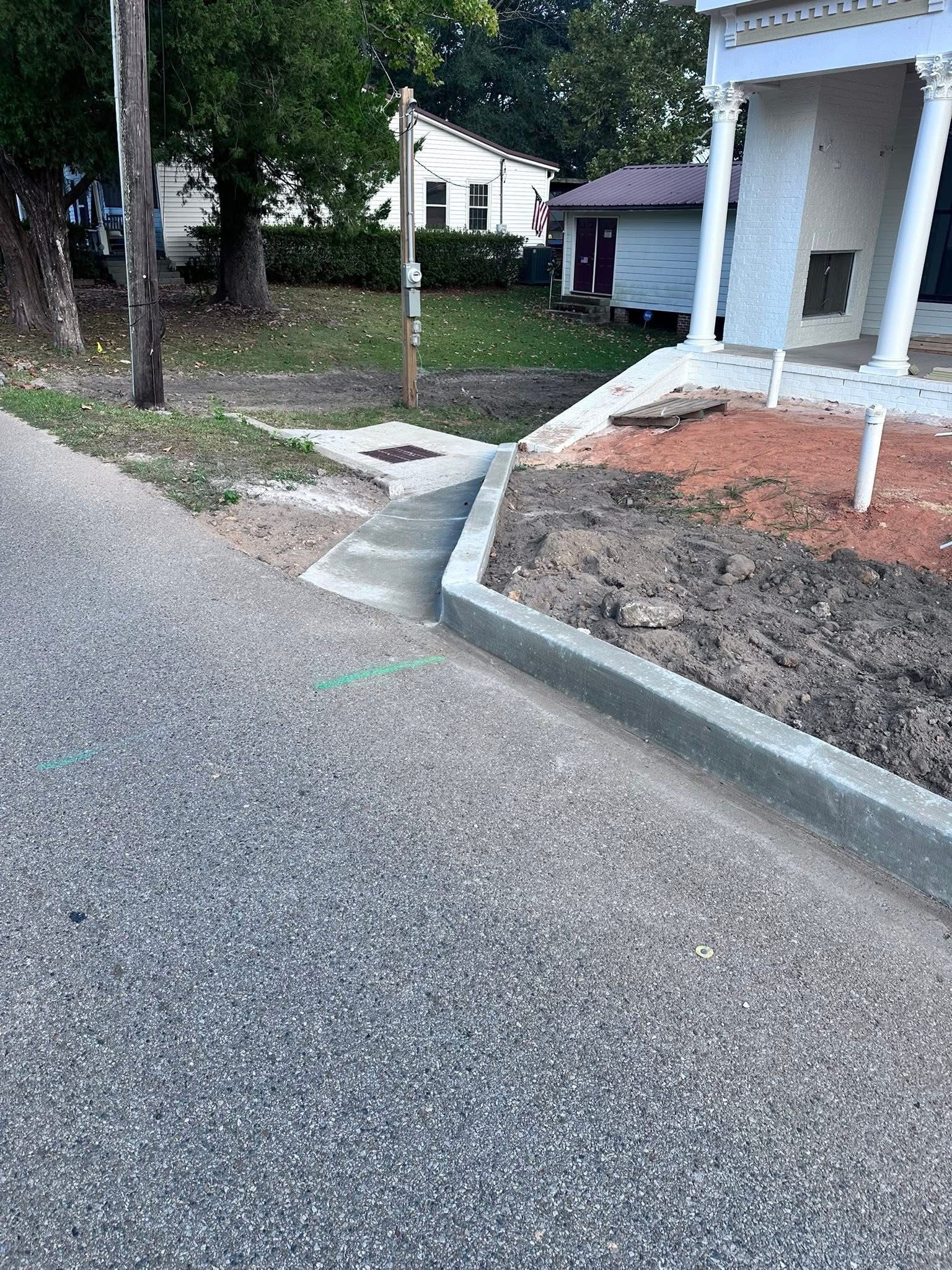 Residential driveway curb and sidewalk by a house, with a small ramp and landscaped yard.