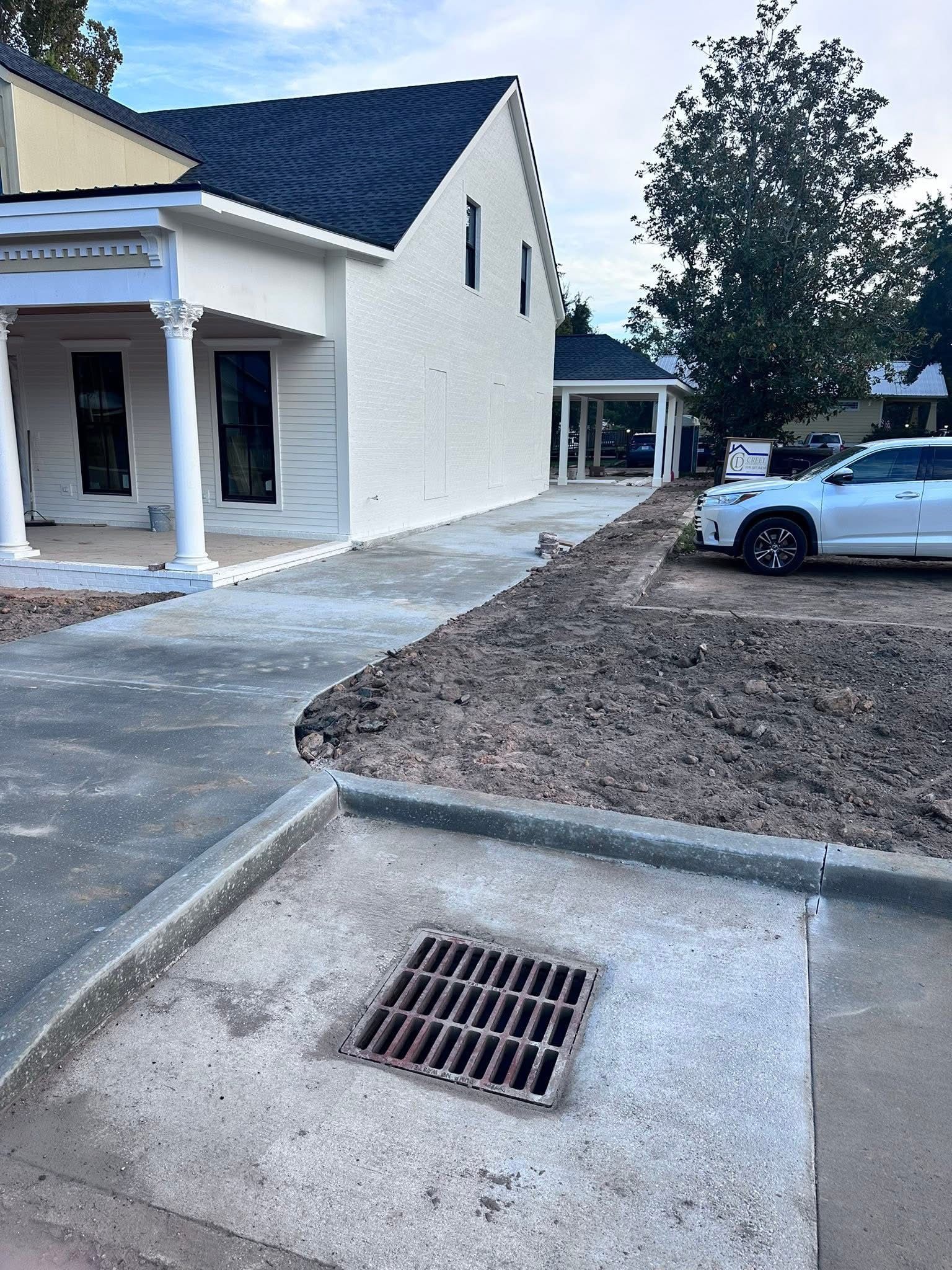 Construction site with a building entrance, fresh concrete curb, drain grate, dirt lot, and parked white car