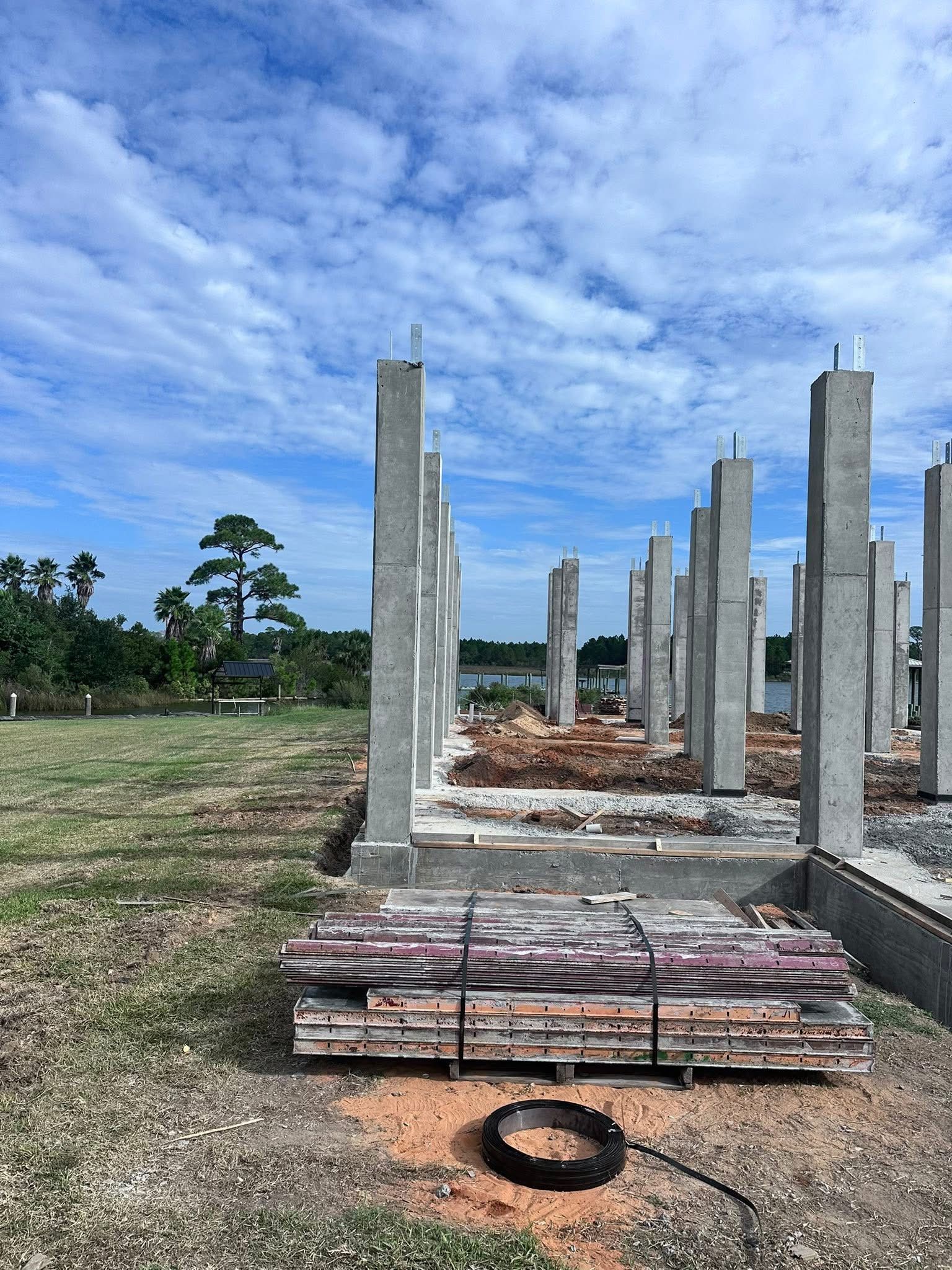 Concrete pillars under construction in a field, with stacked materials in front and a cloudy blue sky.