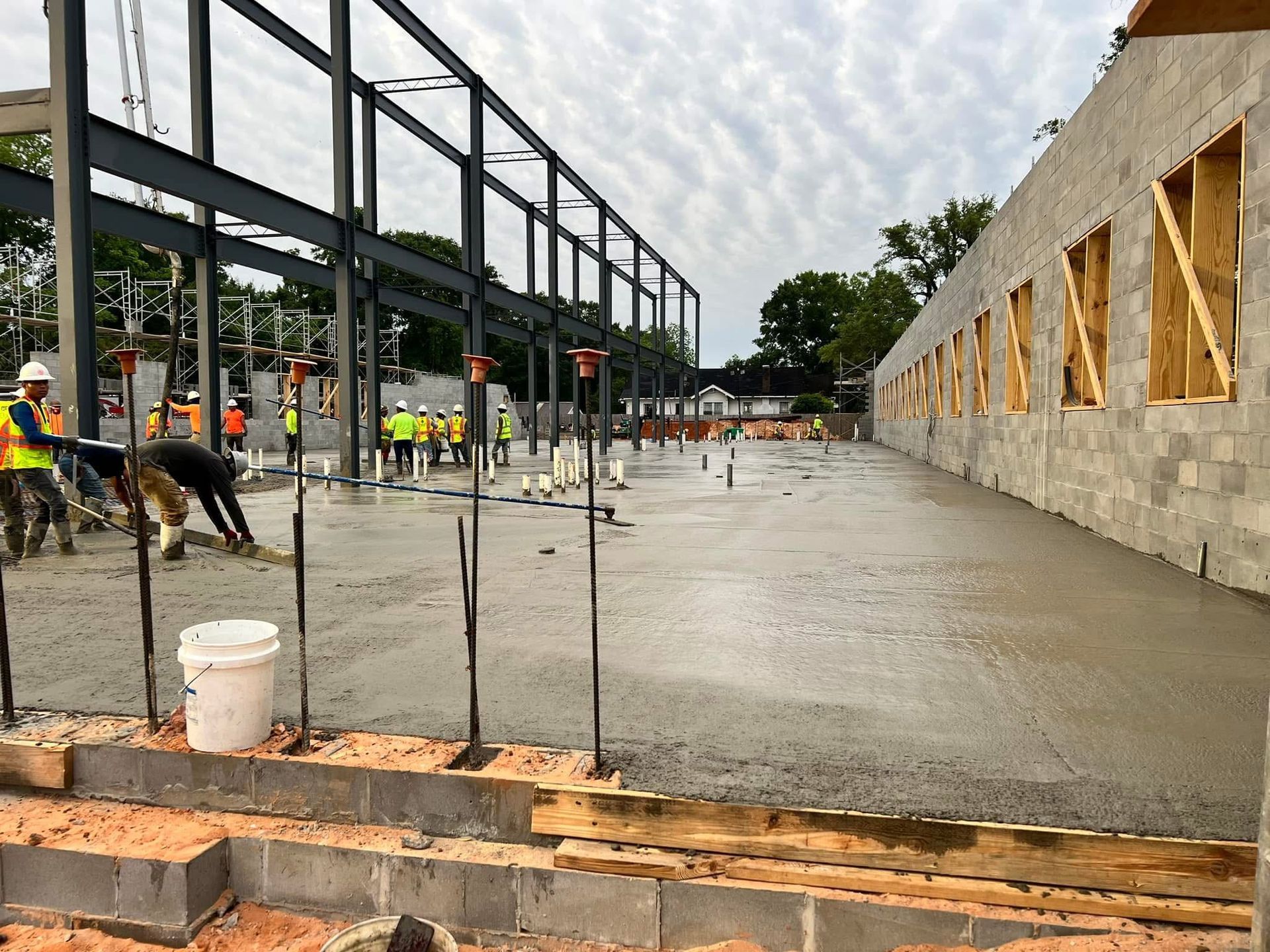 Construction workers pouring a concrete slab beside a steel frame and cinder block building