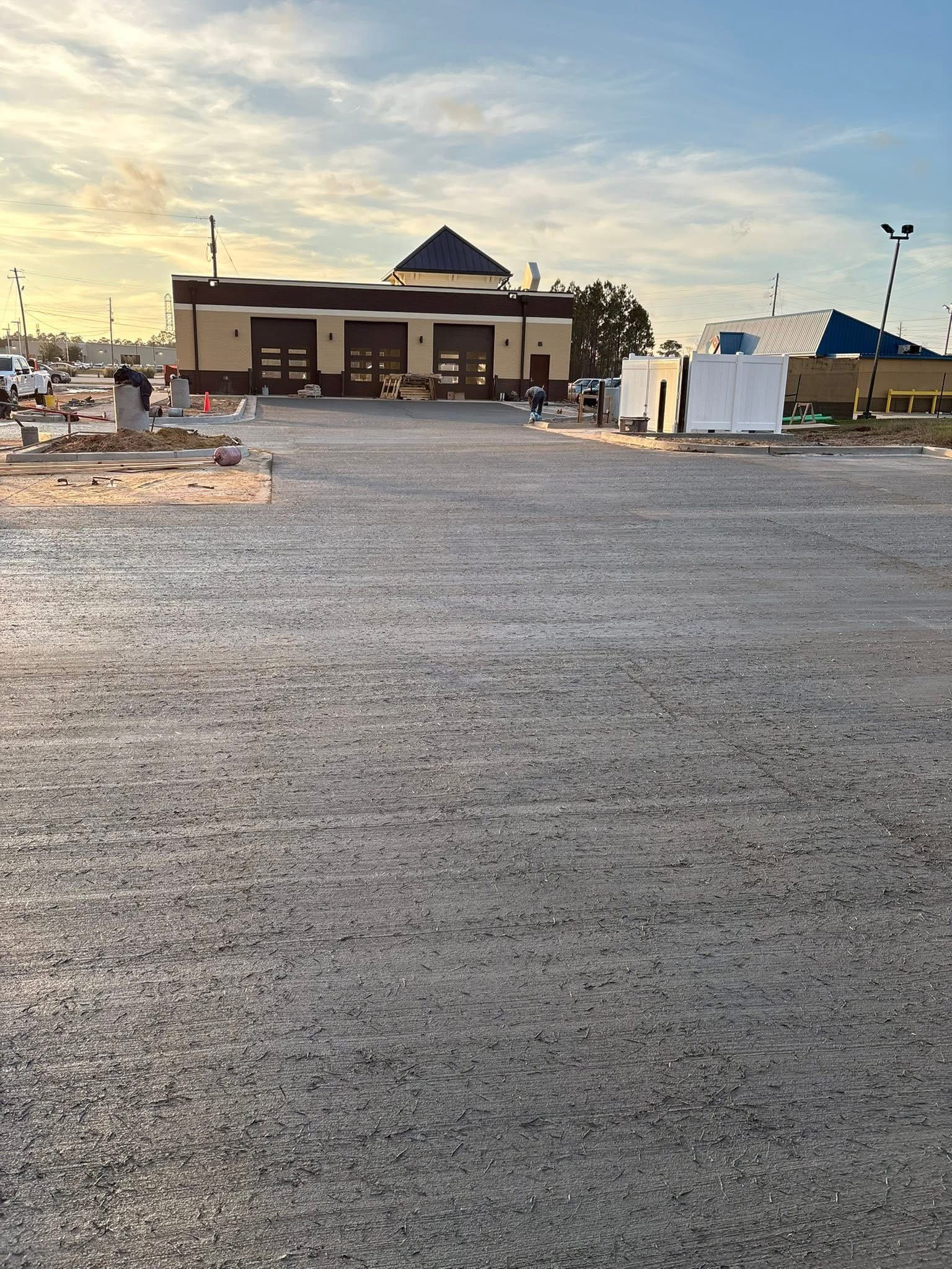 Wide gravel lot leading to a small building at sunset, with scattered utility boxes and poles.