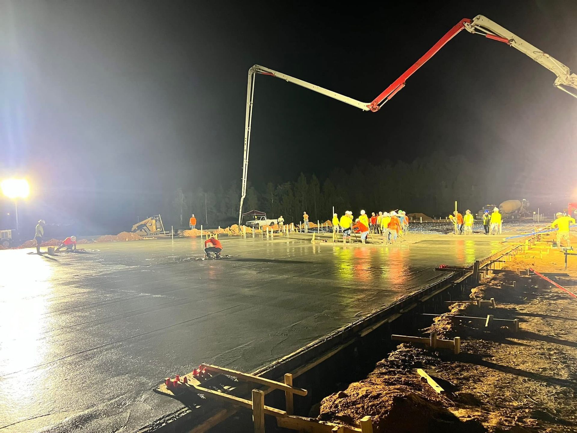 Nighttime construction site with workers and a concrete pump pouring across a wet road