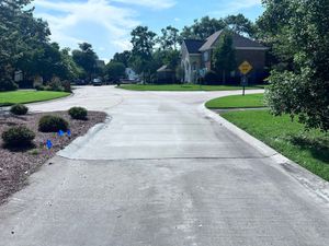 Quiet suburban street with a curving concrete road, green lawns, trees, and houses under a sunny sky