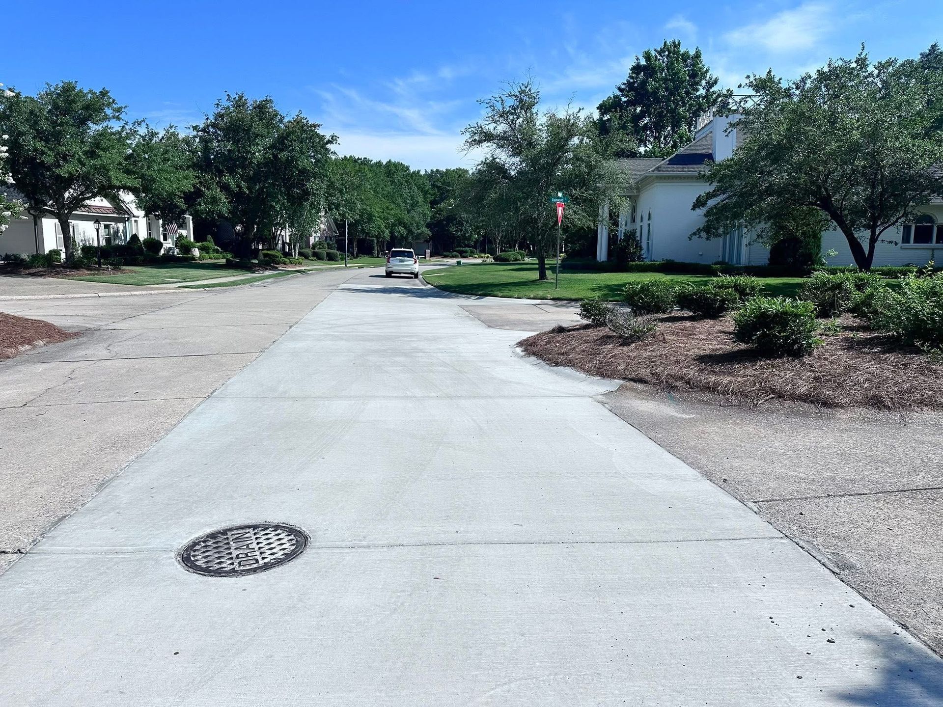 Concrete sidewalk through a quiet residential neighborhood with trees, houses, and a manhole cover nearby