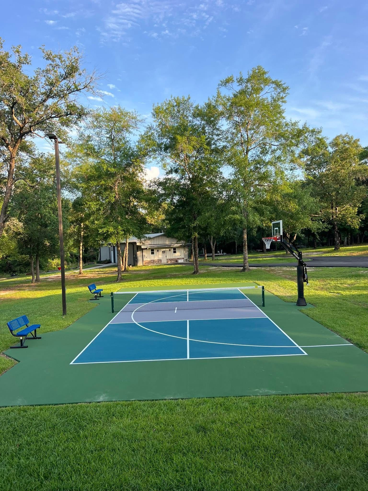 Outdoor basketball court in a green park, with blue and green painted surface and trees around it