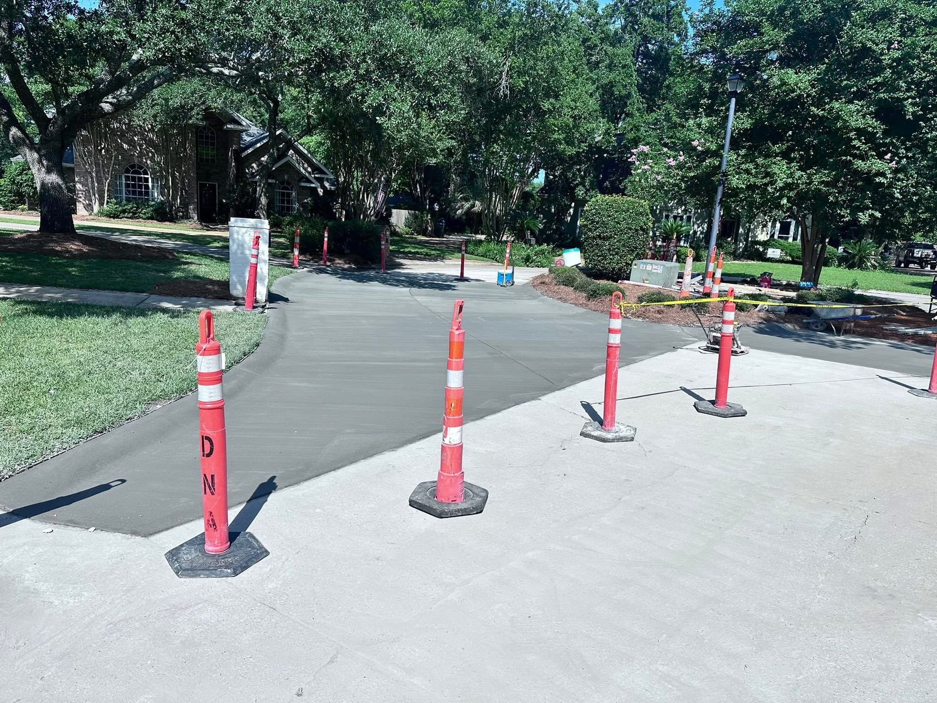 Red traffic cones block a paved park path beside trees and landscaping.