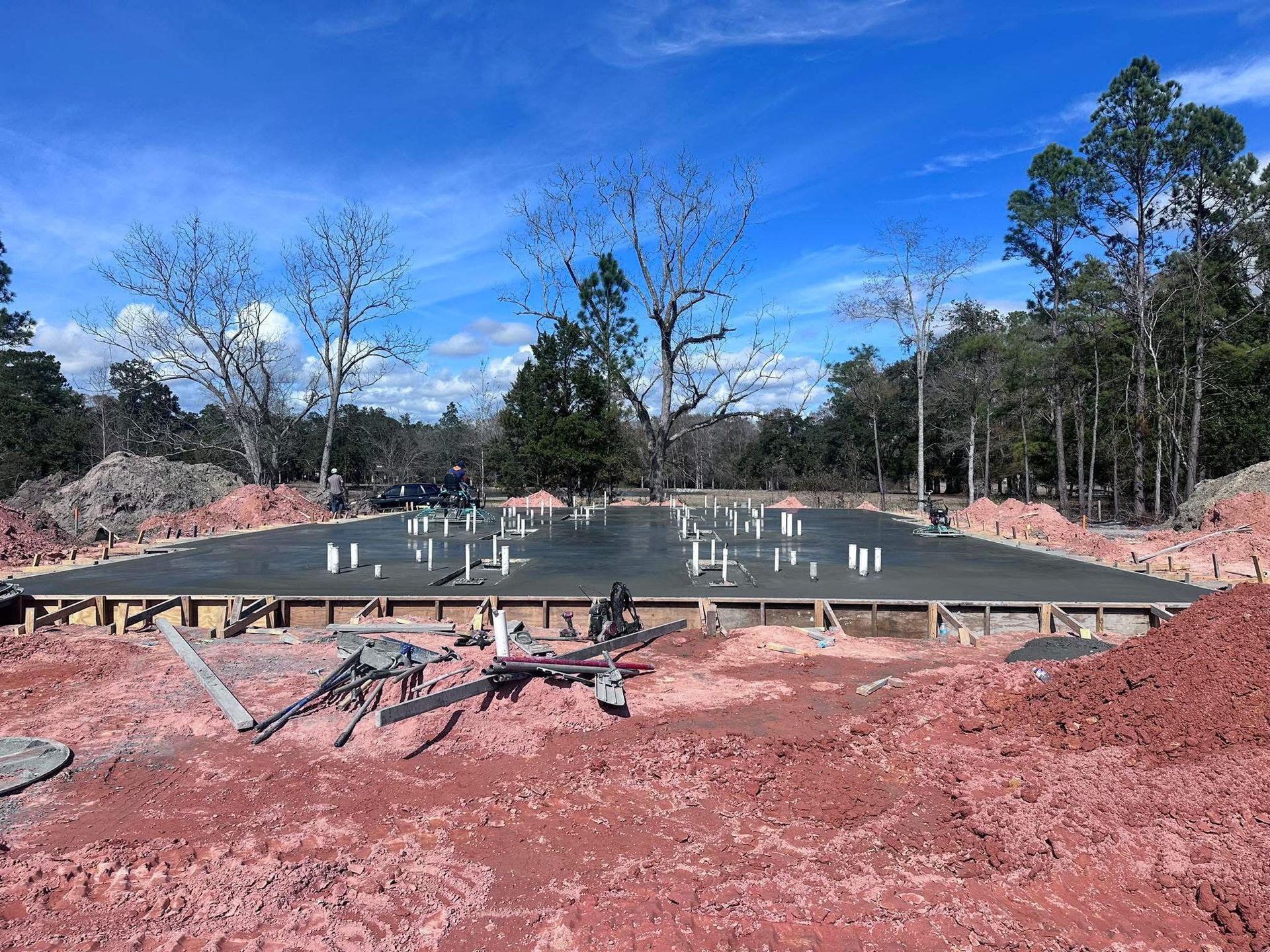 Concrete foundation under construction on red dirt with trees and blue sky in the background
