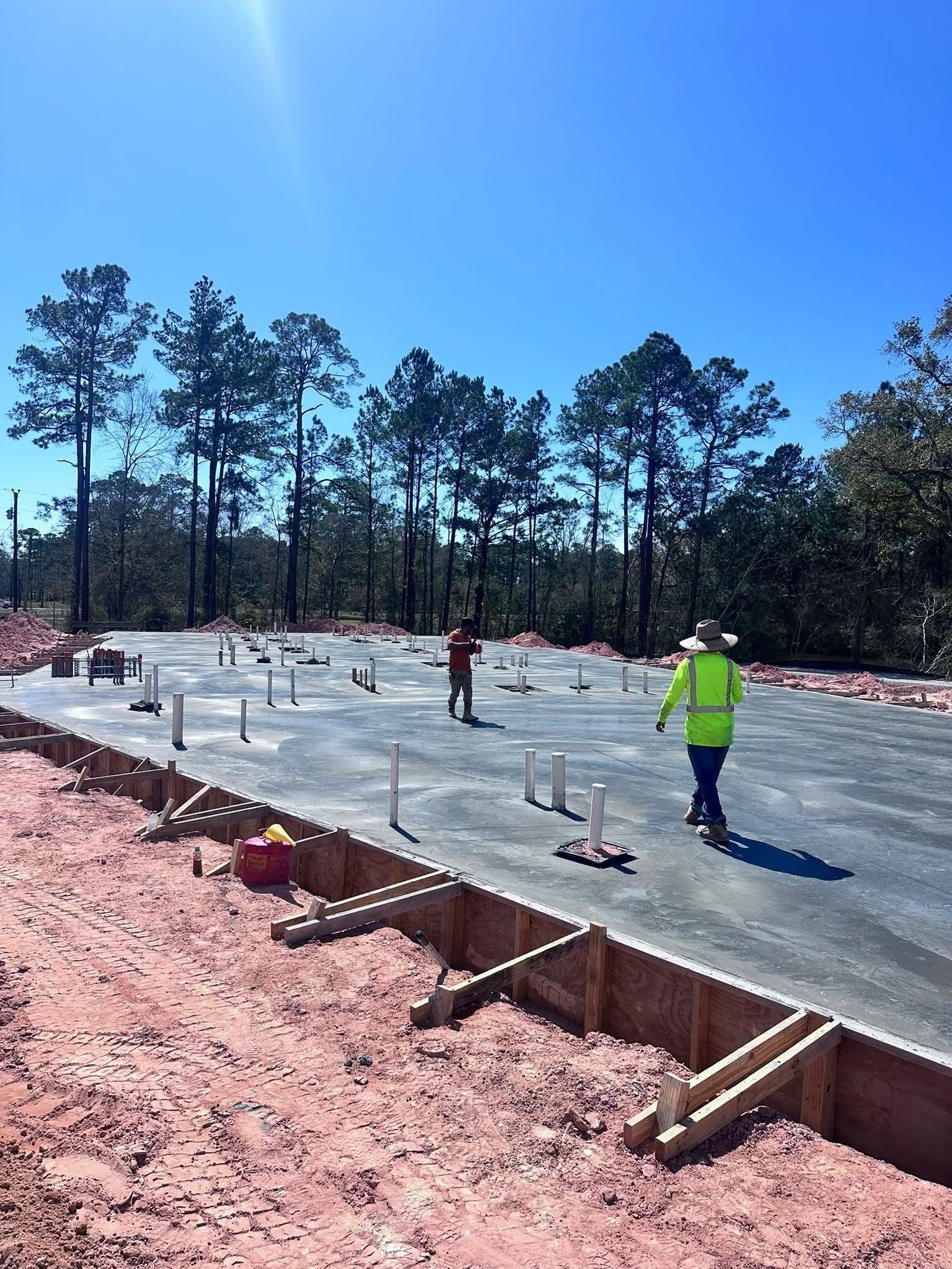 Construction site with a concrete slab, rebar stubs, and workers in safety vests under a clear blue sky