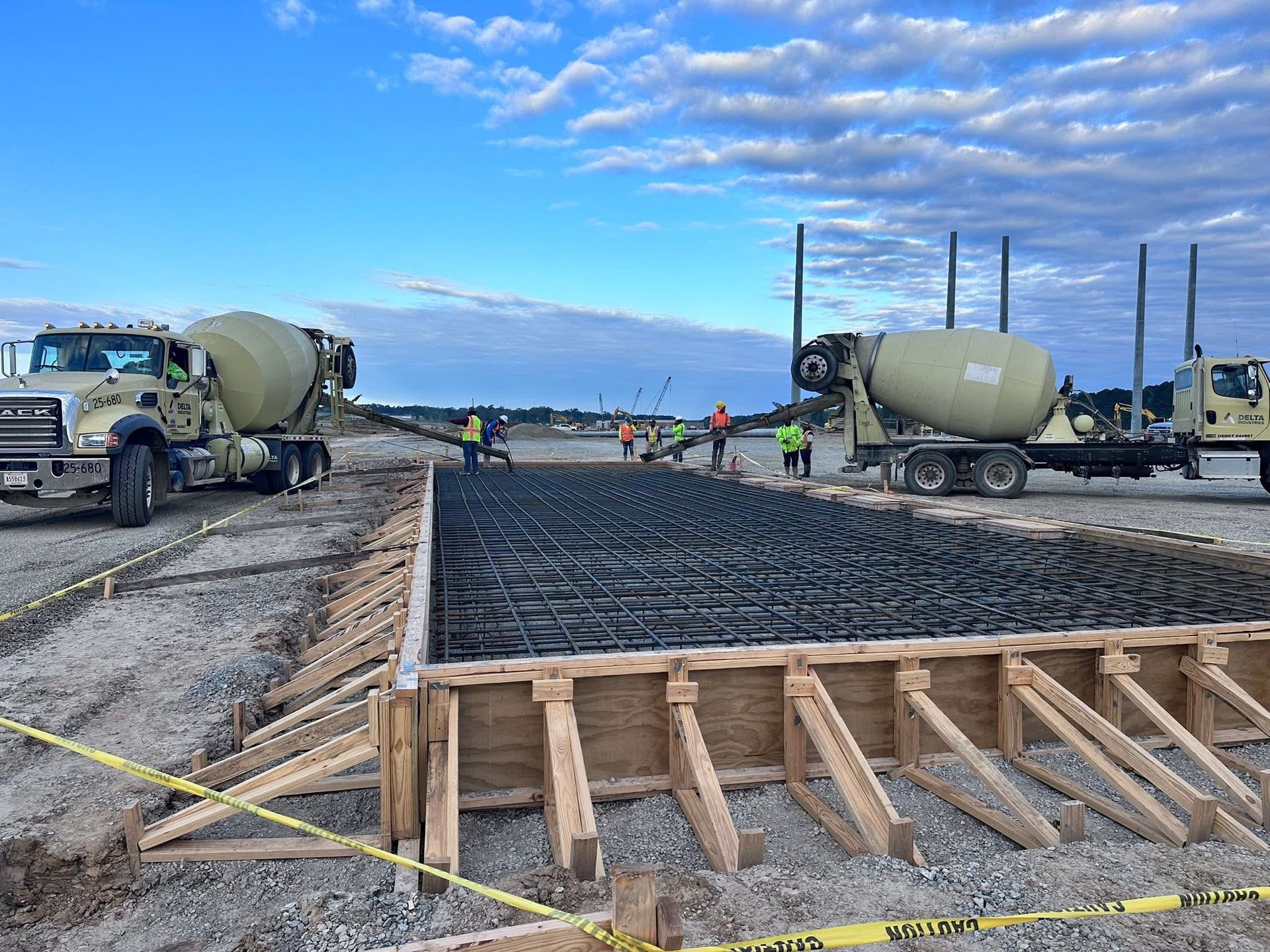 Concrete trucks and workers pouring a road slab at a construction site under a cloudy sky