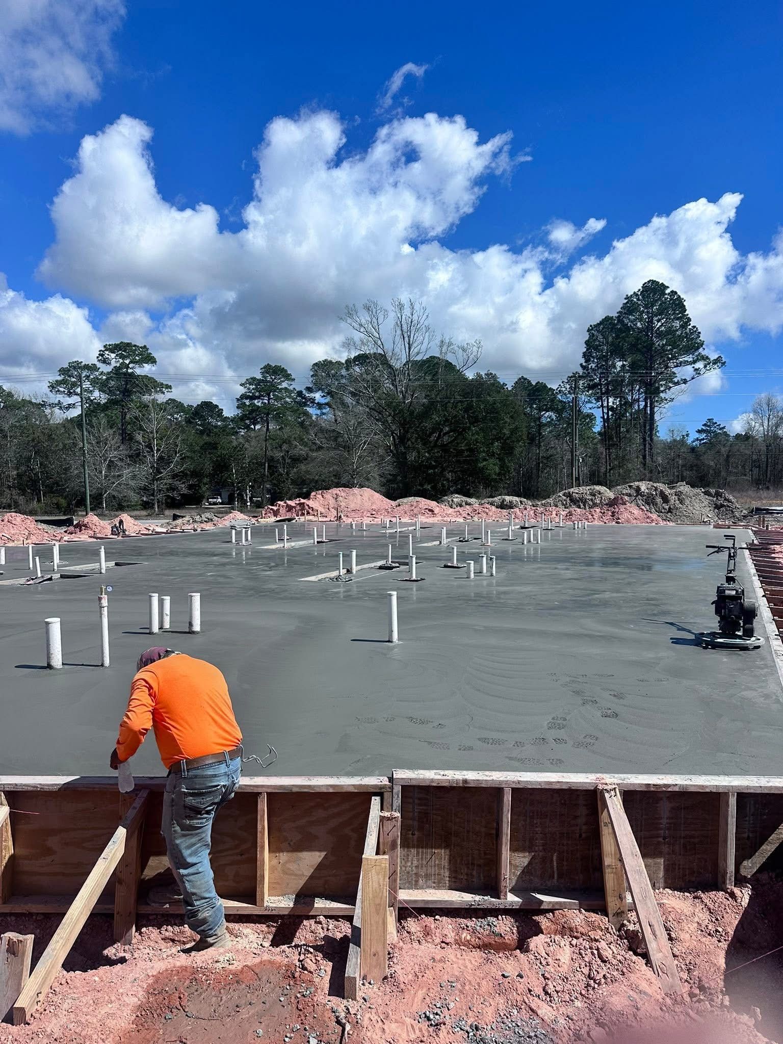 Construction worker in orange shirt pouring concrete for a slab under a bright cloudy sky