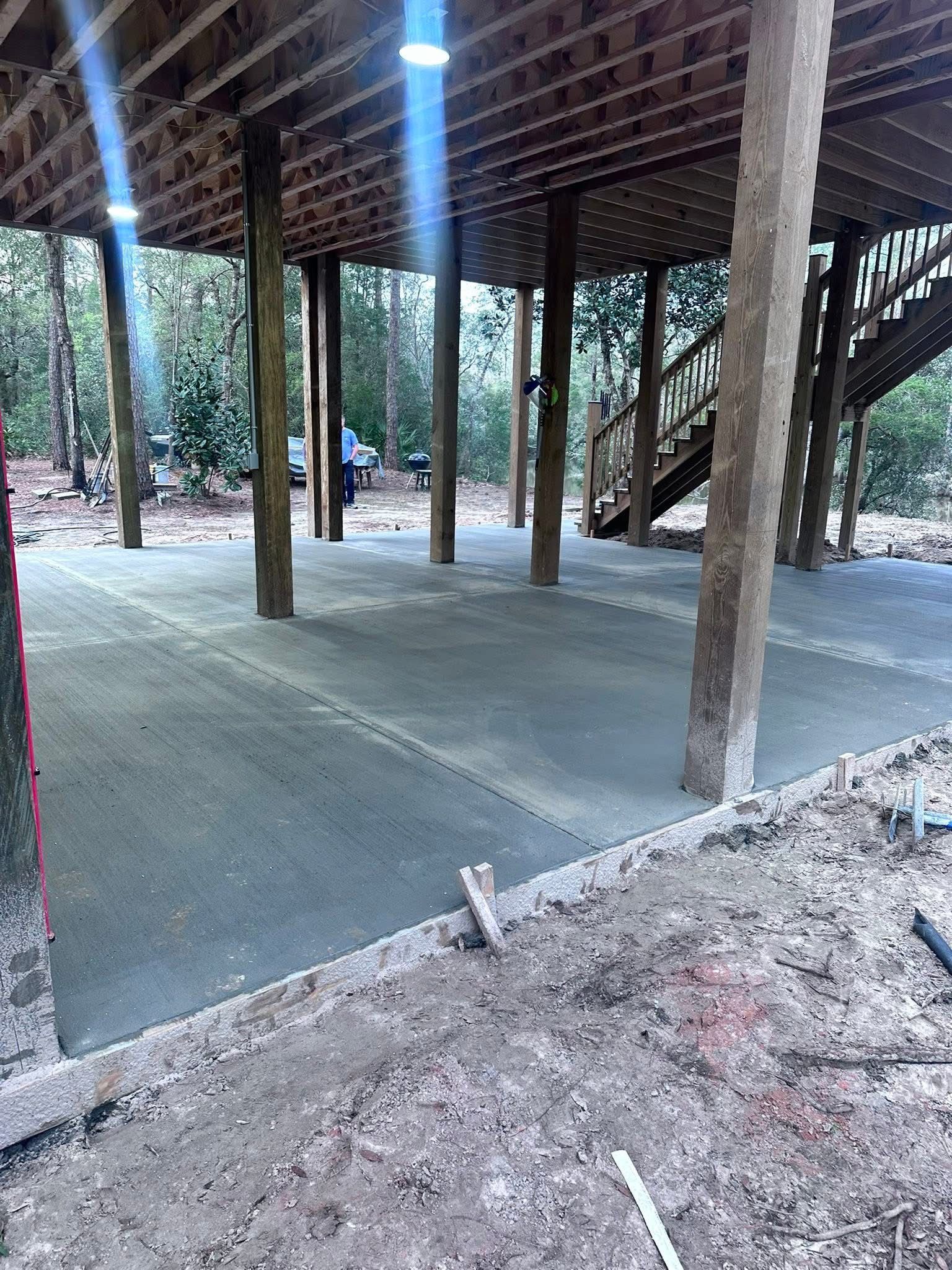 Open-air wooden pavilion with concrete floor and support posts in a wooded area