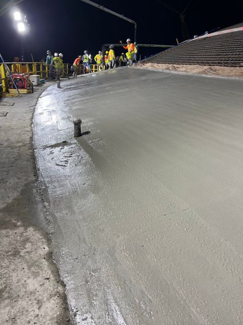 Nighttime construction crew smoothing wet concrete on a curved roadway under bright lights