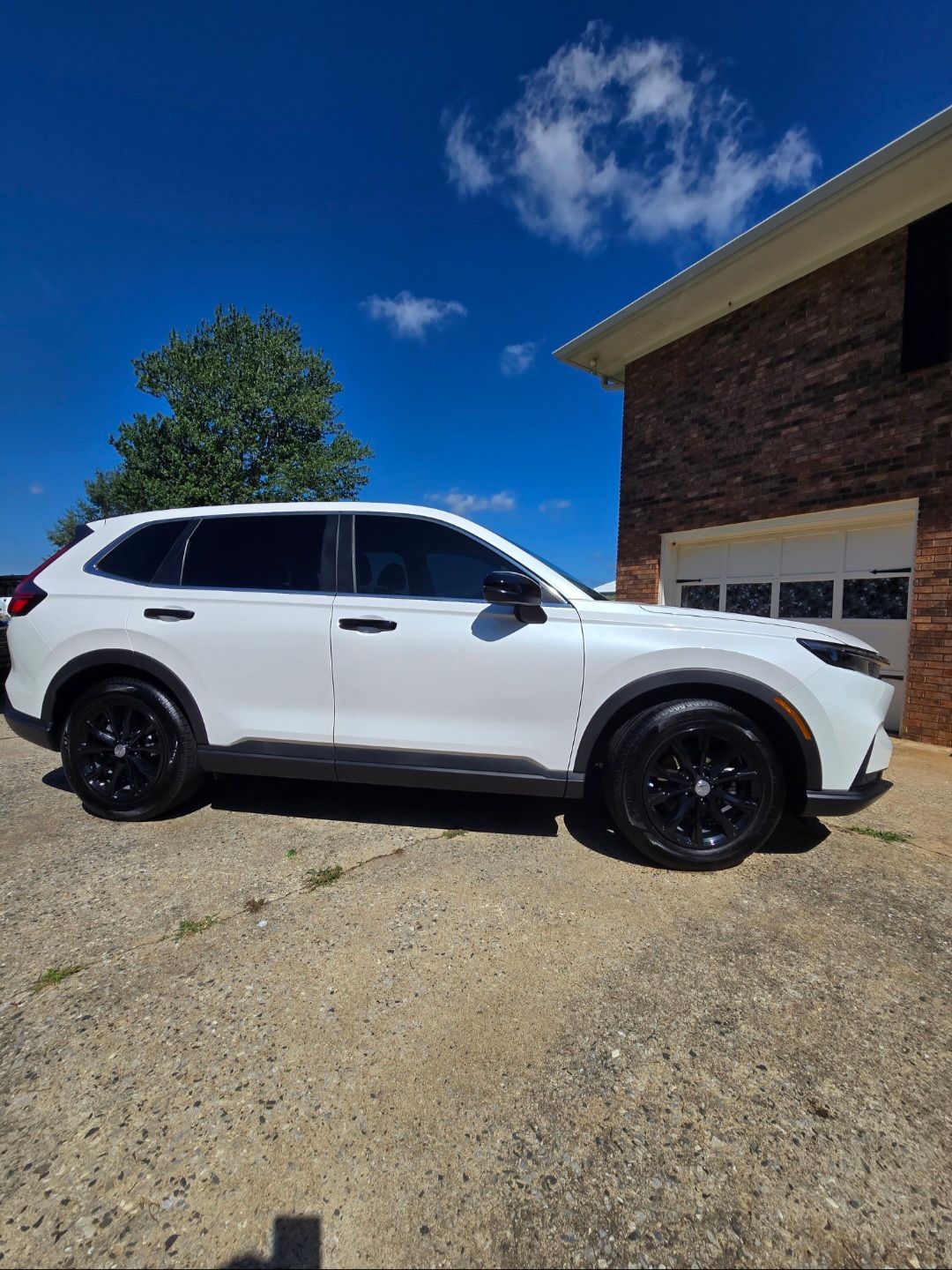 A white SUV with black rims parked on a gravel driveway in front of a brick building under a clear blue sky.