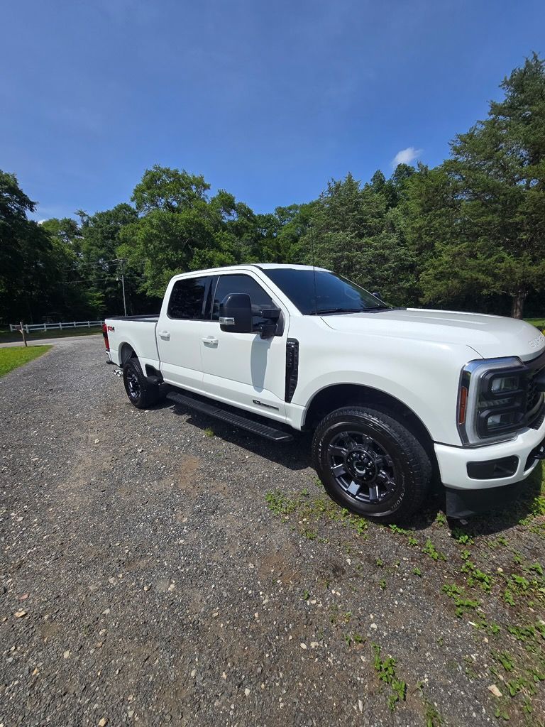 A white Ford Super Duty crew cab truck parked on a gravel driveway under a clear blue sky.