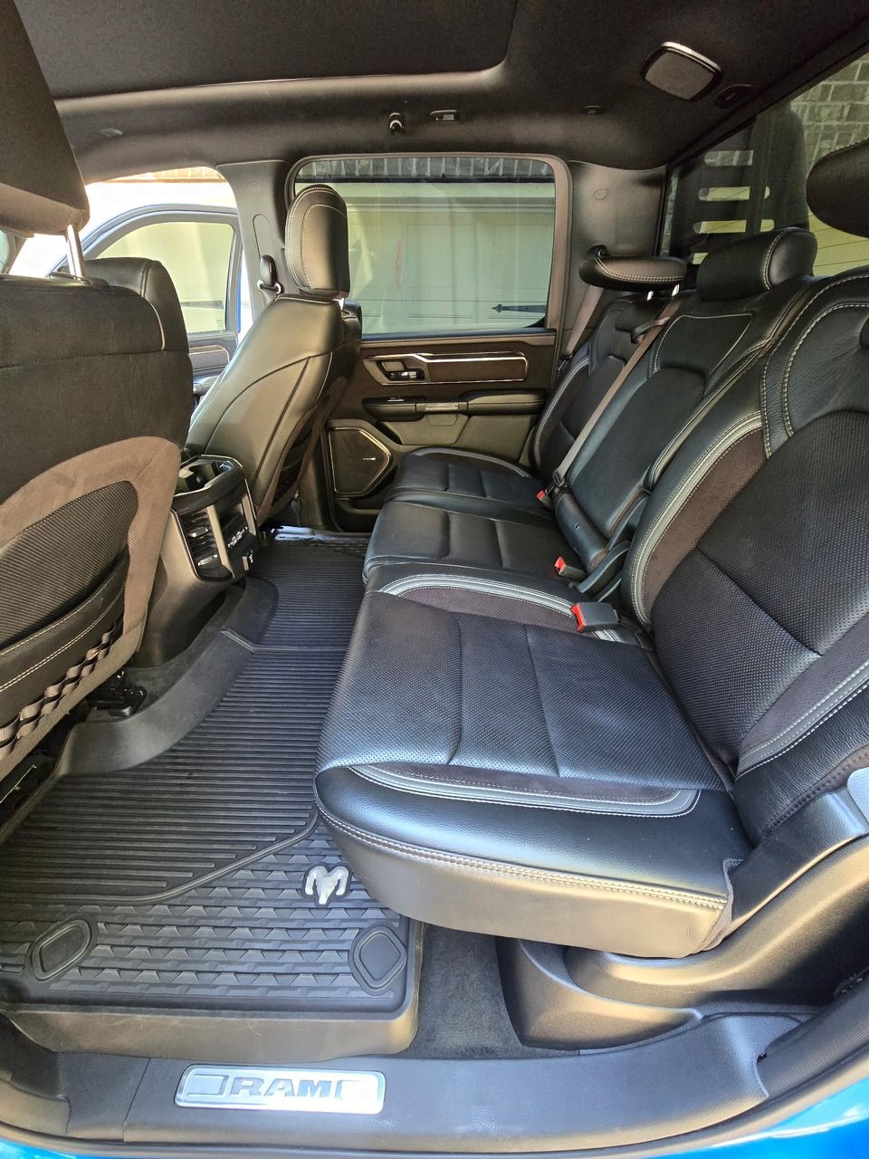 The spacious back seat area of a Ram truck featuring black leather upholstery and rubber floor mats.
