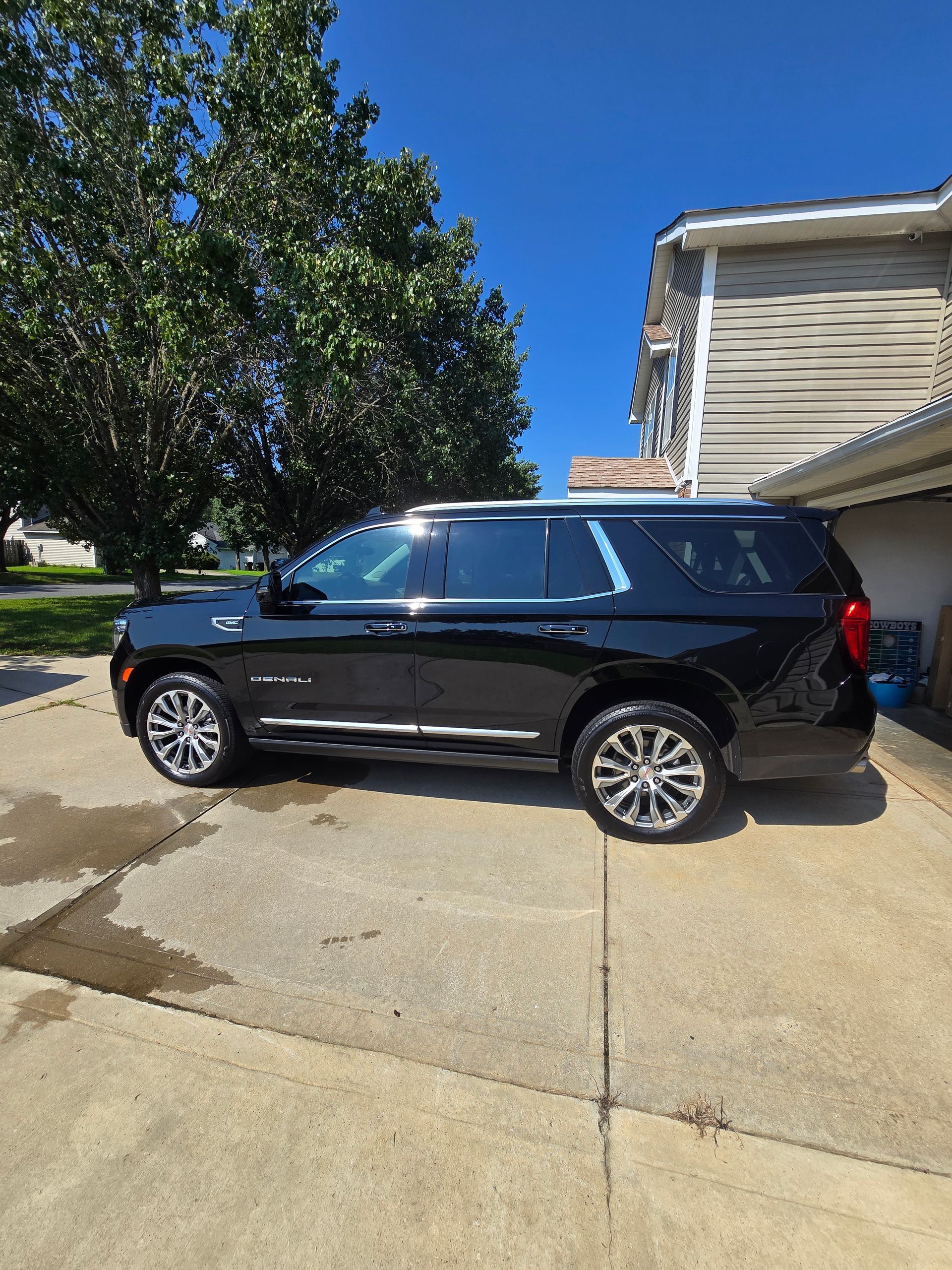 A black Chevrolet Tahoe SUV parked on a concrete driveway next to a residential house on a sunny day.