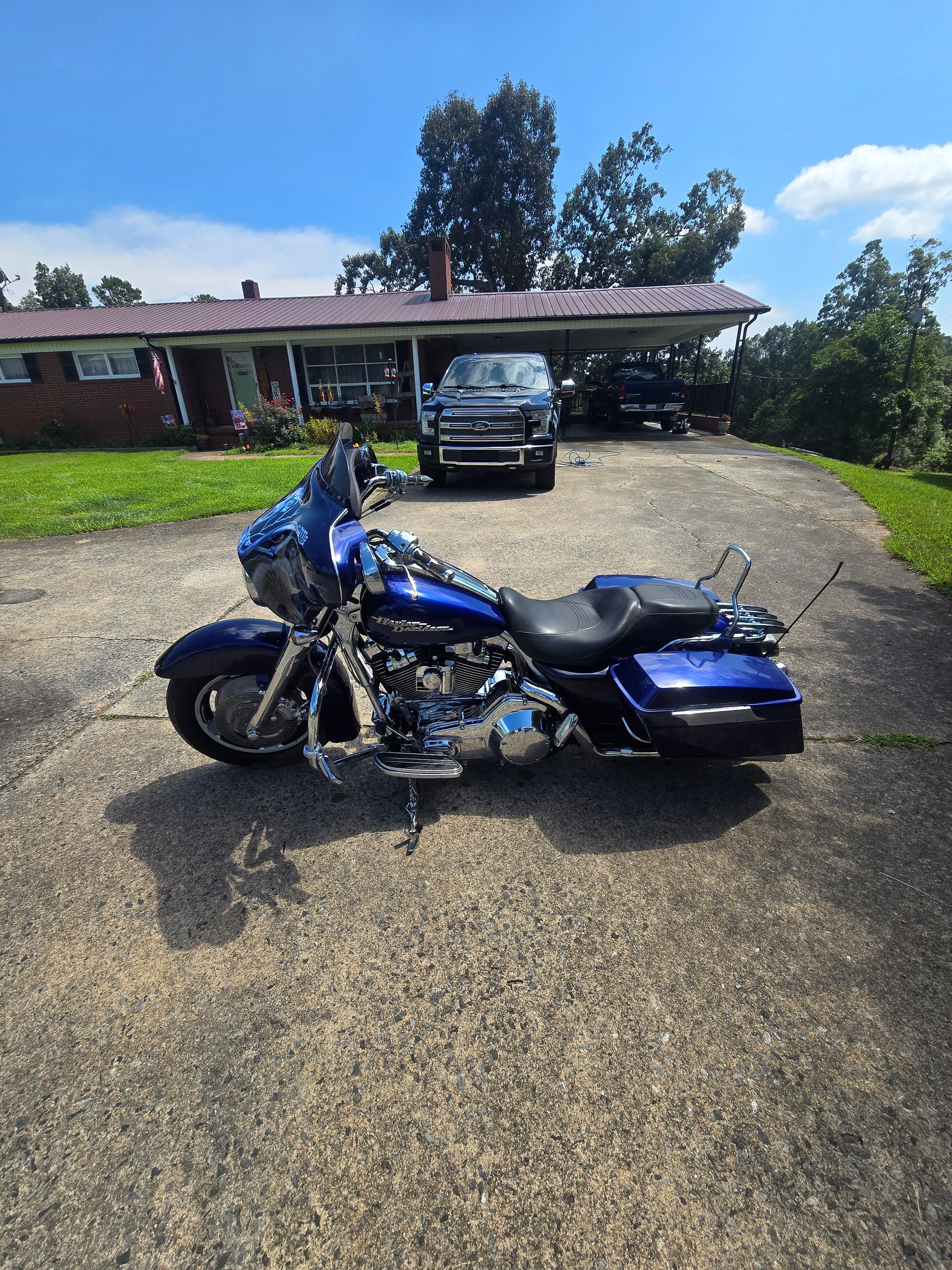 A blue Harley-Davidson motorcycle parked on a gravel driveway in front of a house on a sunny day.