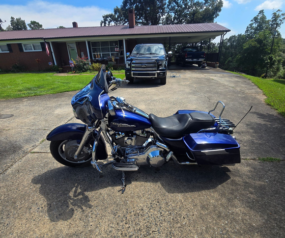 A glossy blue Harley-Davidson touring motorcycle parked on a residential driveway in front of a house and truck.