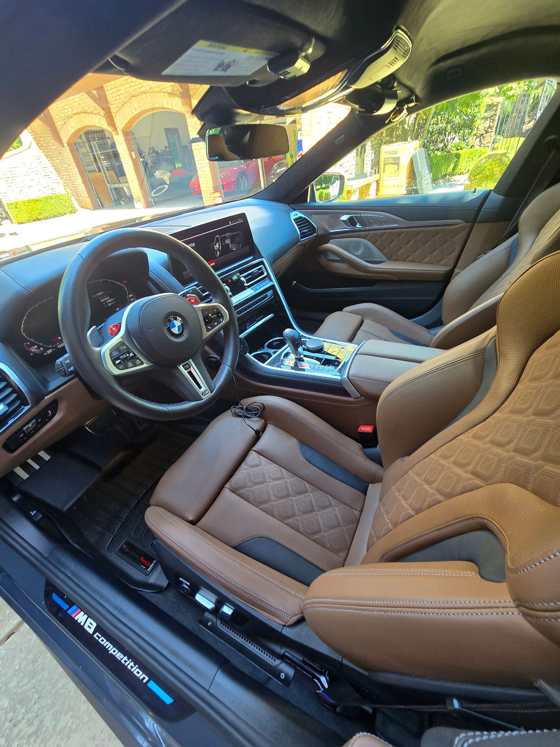 The interior of a BMW M8 with quilted brown leather bucket seats, a leather-wrapped steering wheel, and a digital dash.