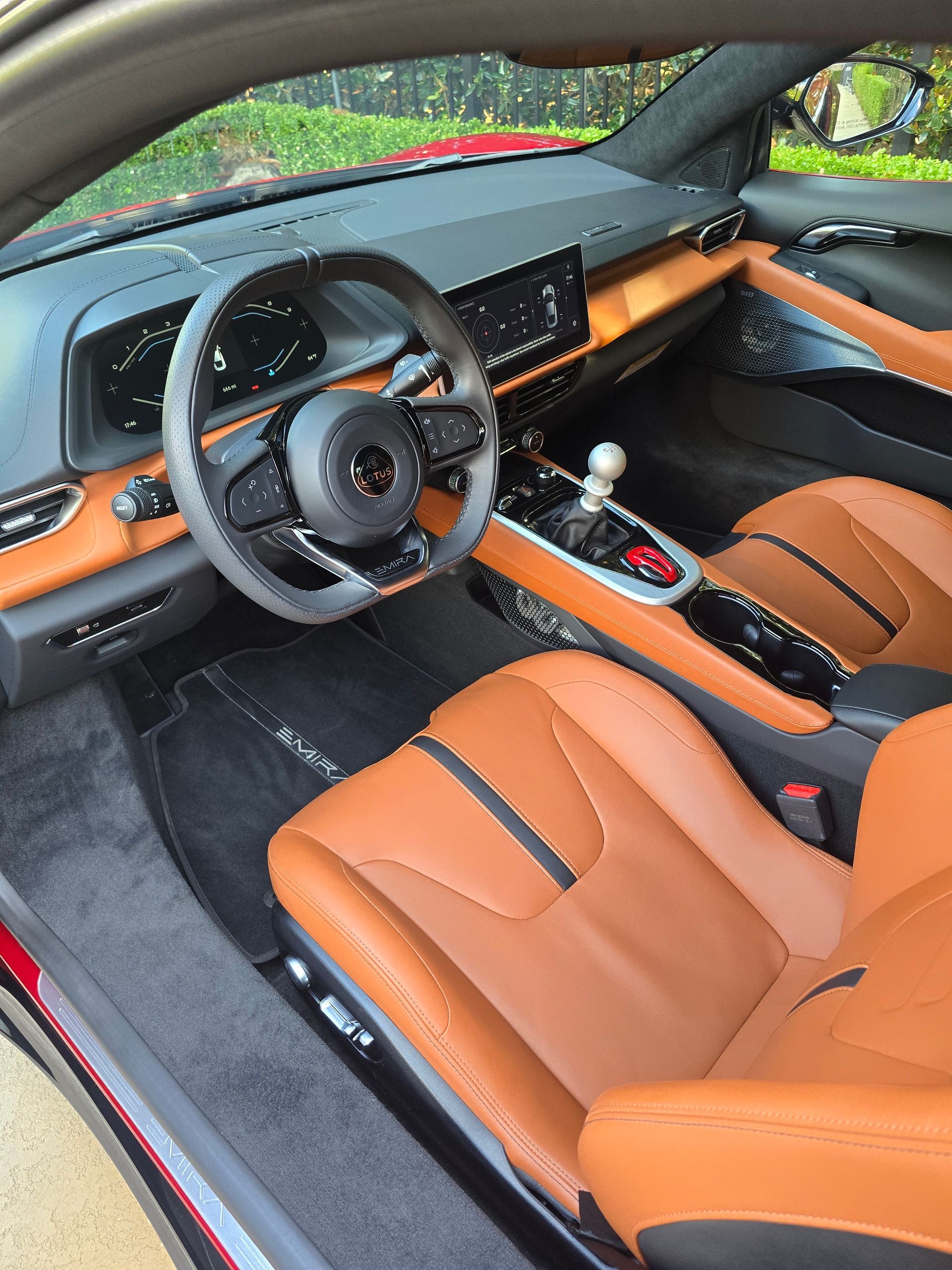 The interior of a modern car with brown leather bucket seats, a black dashboard, and a manual gear shifter.
