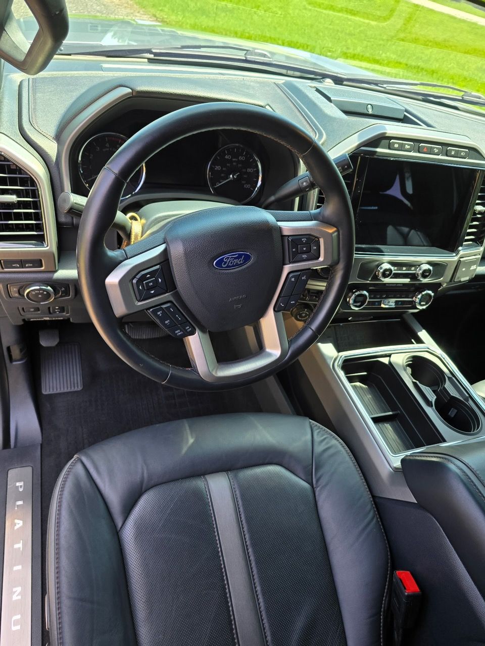 Interior view of a Ford F-150 Platinum featuring a black leather steering wheel, dashboard, and driver seat.