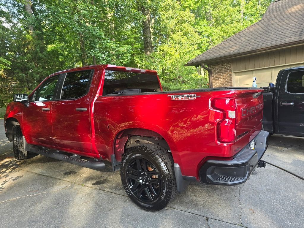 A red Chevrolet Silverado pickup truck parked on a driveway next to a house and a black truck.