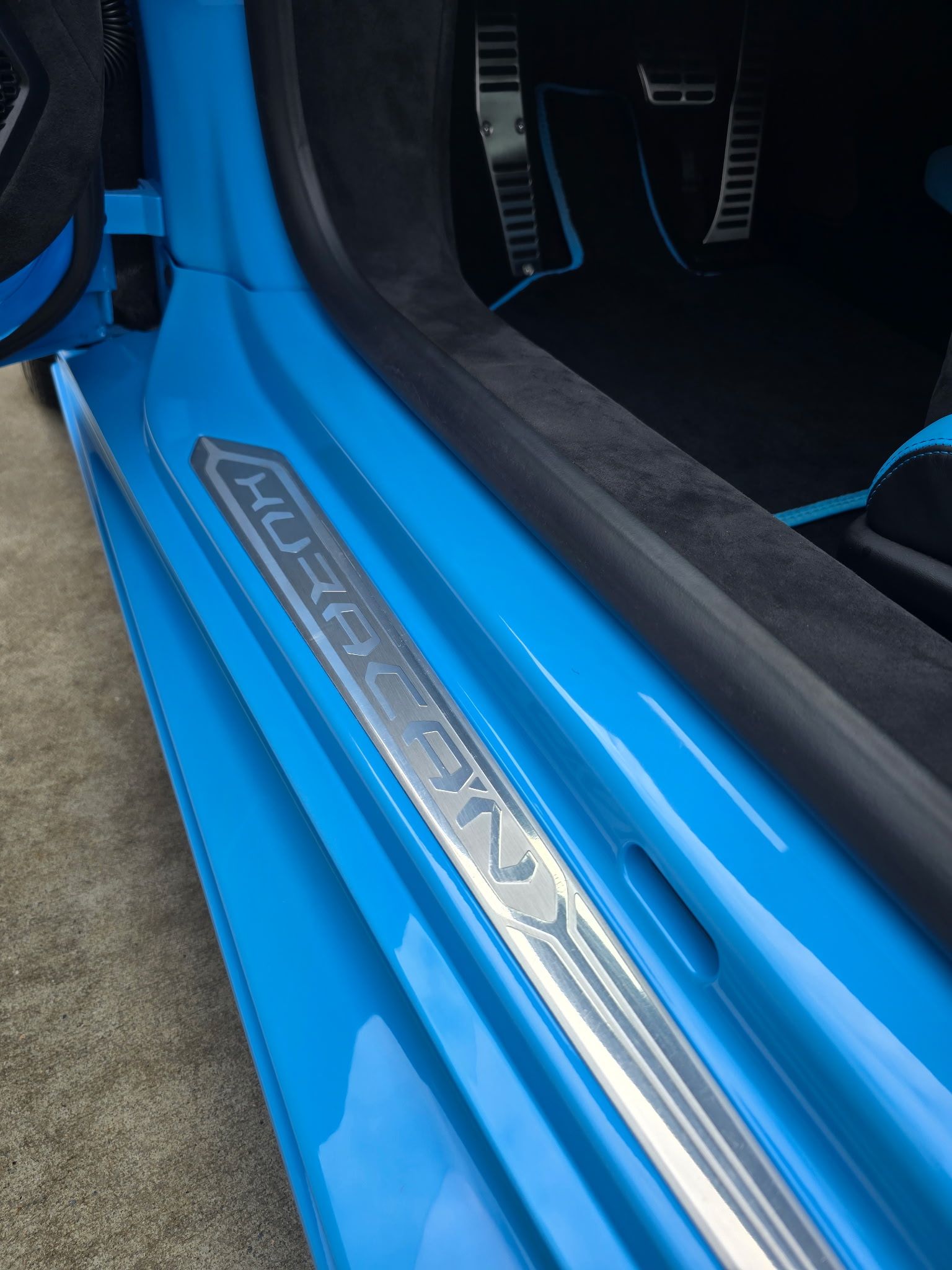 Close-up of a blue Lamborghini Huracán door sill plate with silver lettering, leading into the car's interior.