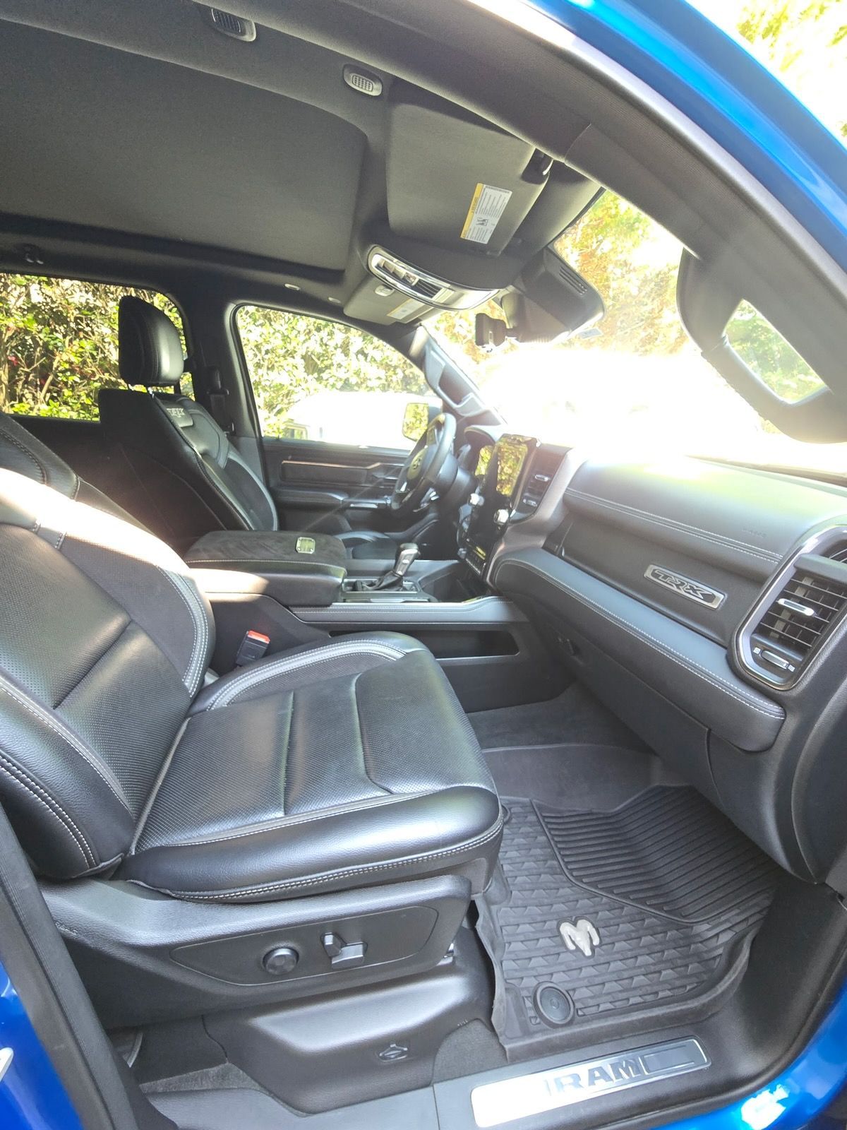 The interior of a blue truck featuring black leather seats, a digital dashboard, and Ram-branded floor mats.
