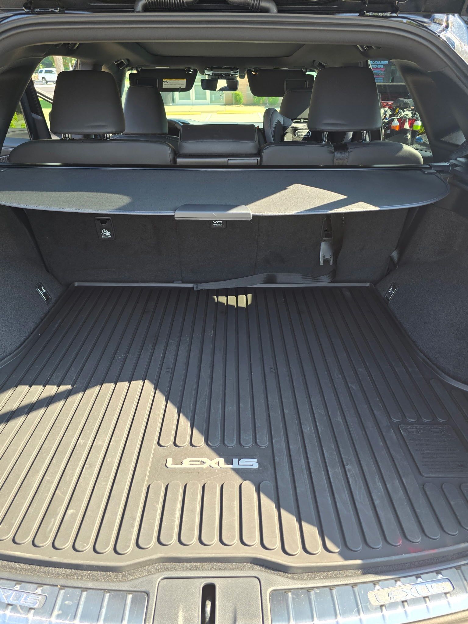The trunk of a Lexus SUV with a black rubber cargo mat, retractable privacy cover, and a view into the back seat.