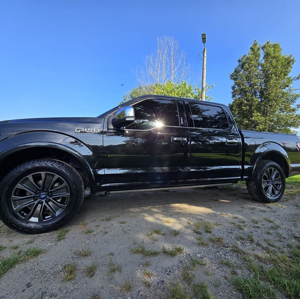 A black Ford F-150 crew cab pickup truck parked on a gravel surface outdoors against a clear blue sky.