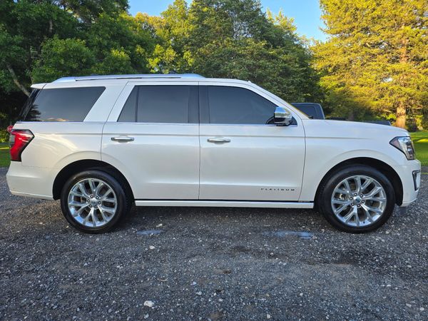 A white Ford Expedition SUV parked on a gravel surface outdoors with trees in the background.