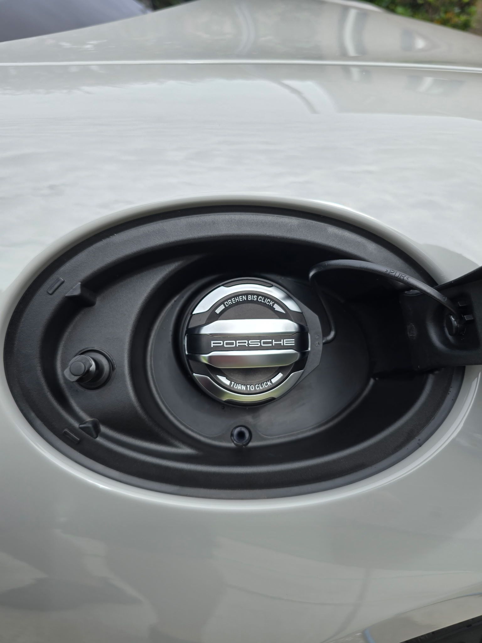 An open fuel filler door on a light-colored vehicle, revealing a metallic, circular gas cap.