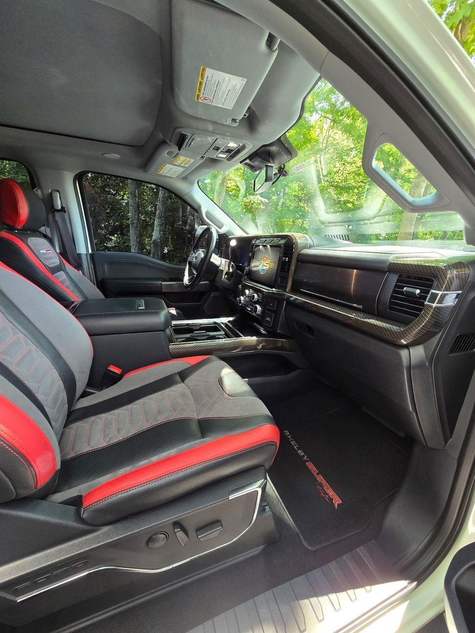 Interior view of a pickup truck with black and red bucket seats, a dashboard, and a floor mat with red trim.