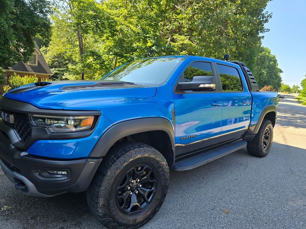 A bright blue Ram TRX pickup truck parked on a paved road with trees in the background.