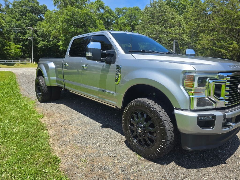 A silver Ford F-Series dually pickup truck parked on a gravel driveway with trees in the background.