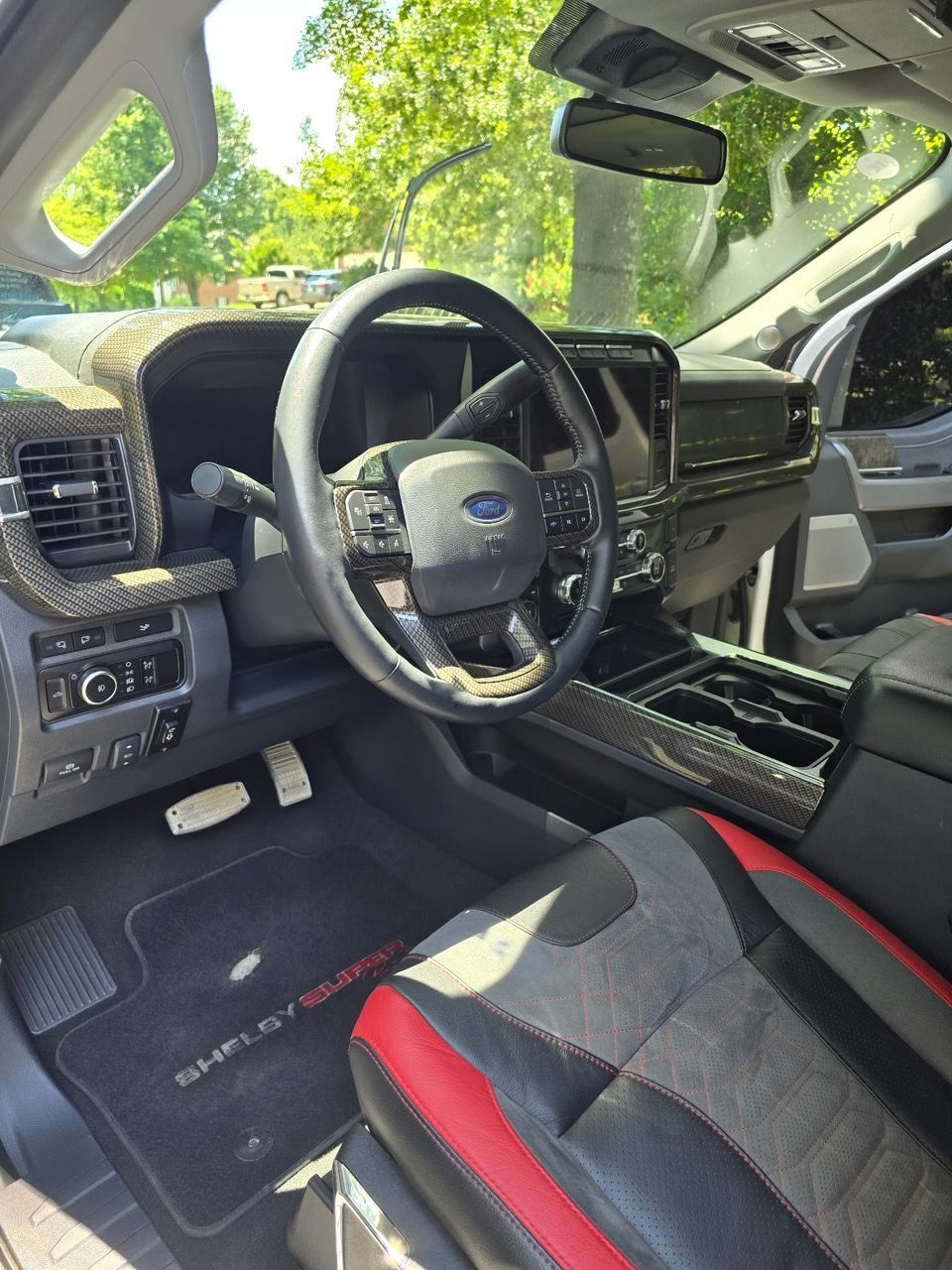 Interior view of a Shelby F-150 featuring a carbon fiber dashboard, black and red leather seats, and branded floor mats.