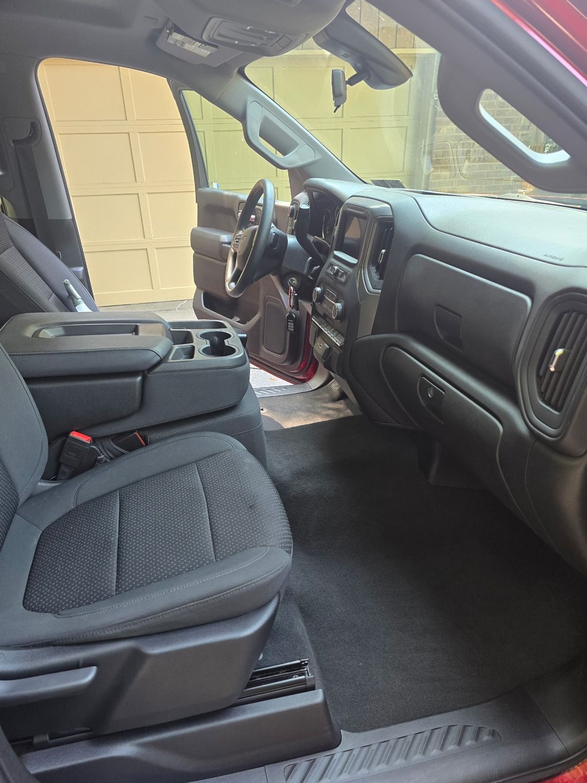 The interior of a vehicle featuring dark grey cloth seats, a black dashboard with a center display, and dark floor mats.