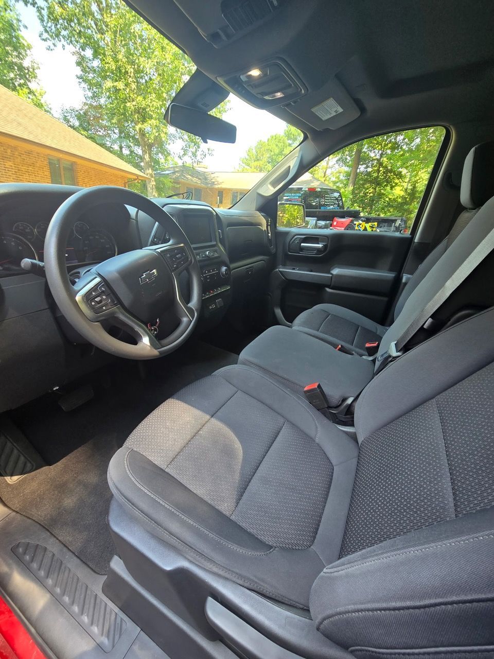 The interior cabin of a vehicle showing gray fabric seats, a steering wheel, and dashboard from the passenger perspective.