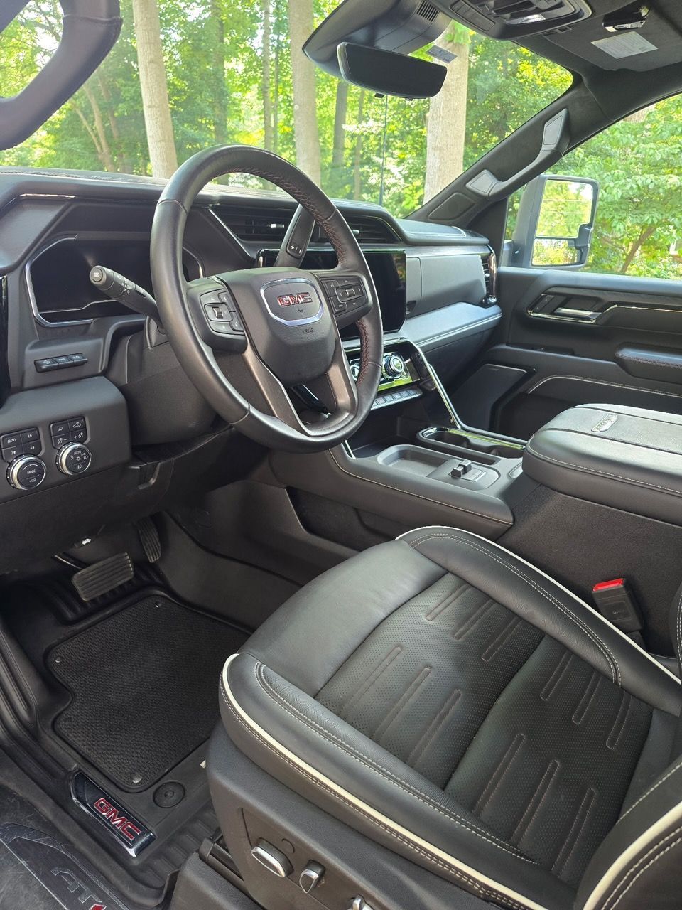 The interior of a black GMC truck featuring a leather steering wheel, bucket seats, and a digital dashboard.
