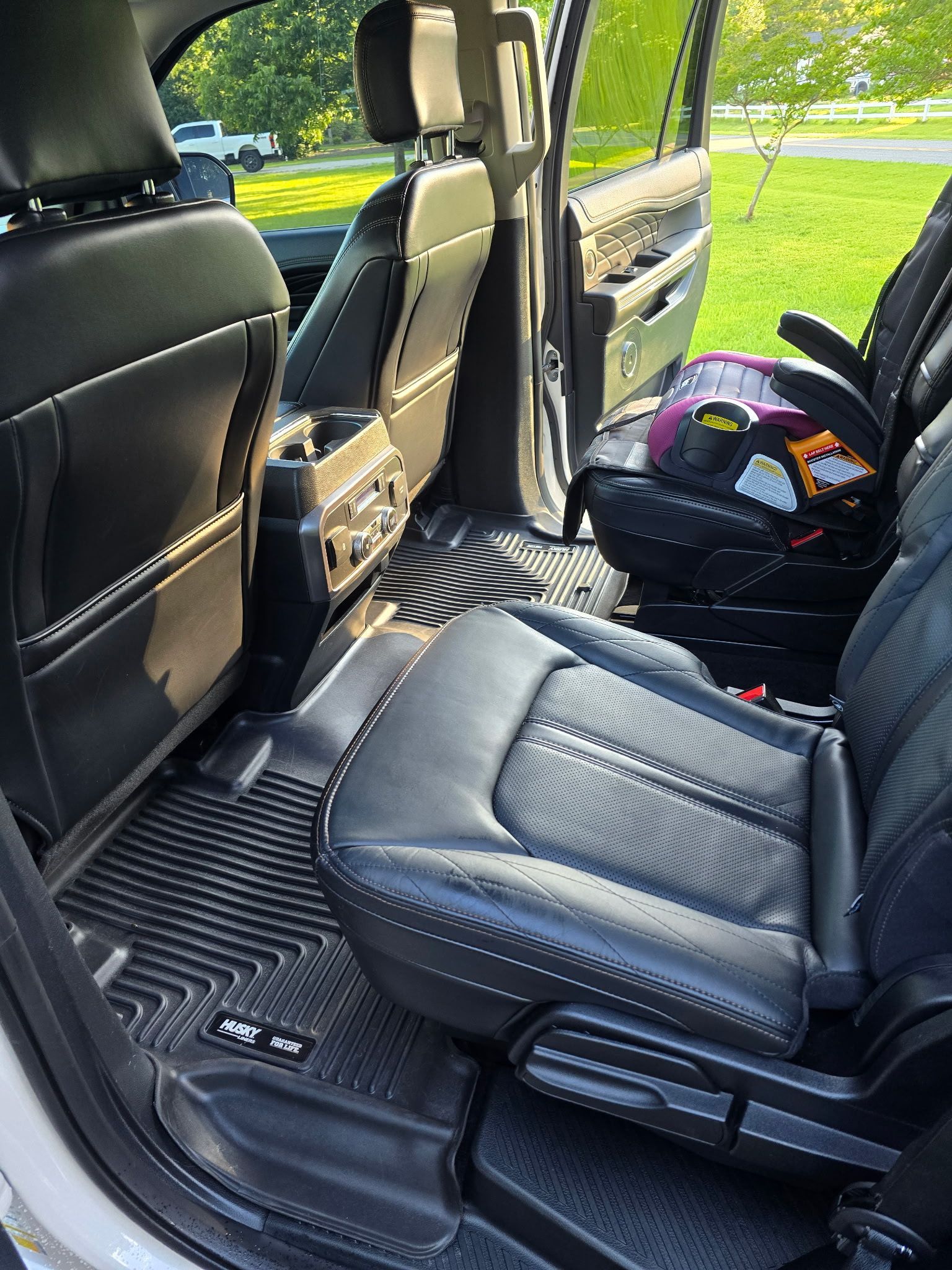 A black leather car interior with dark rubber floor mats, featuring a child car seat secured in the rear.