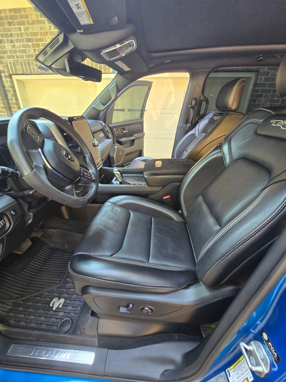 The interior of a blue vehicle, showing a black leather driver's seat, steering wheel, and rubber floor mats.