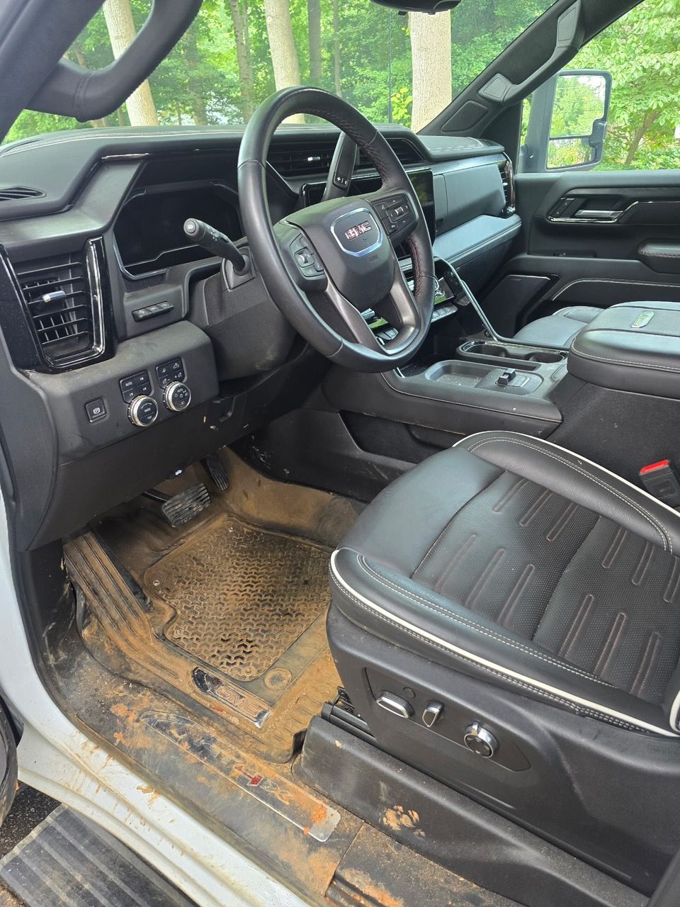 The interior of a vehicle featuring a GMC steering wheel, dark leather seats, and mud-covered floor mats.