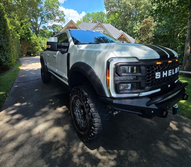 A white Shelby Ford F-250 pickup truck with black racing stripes parked on a residential driveway.