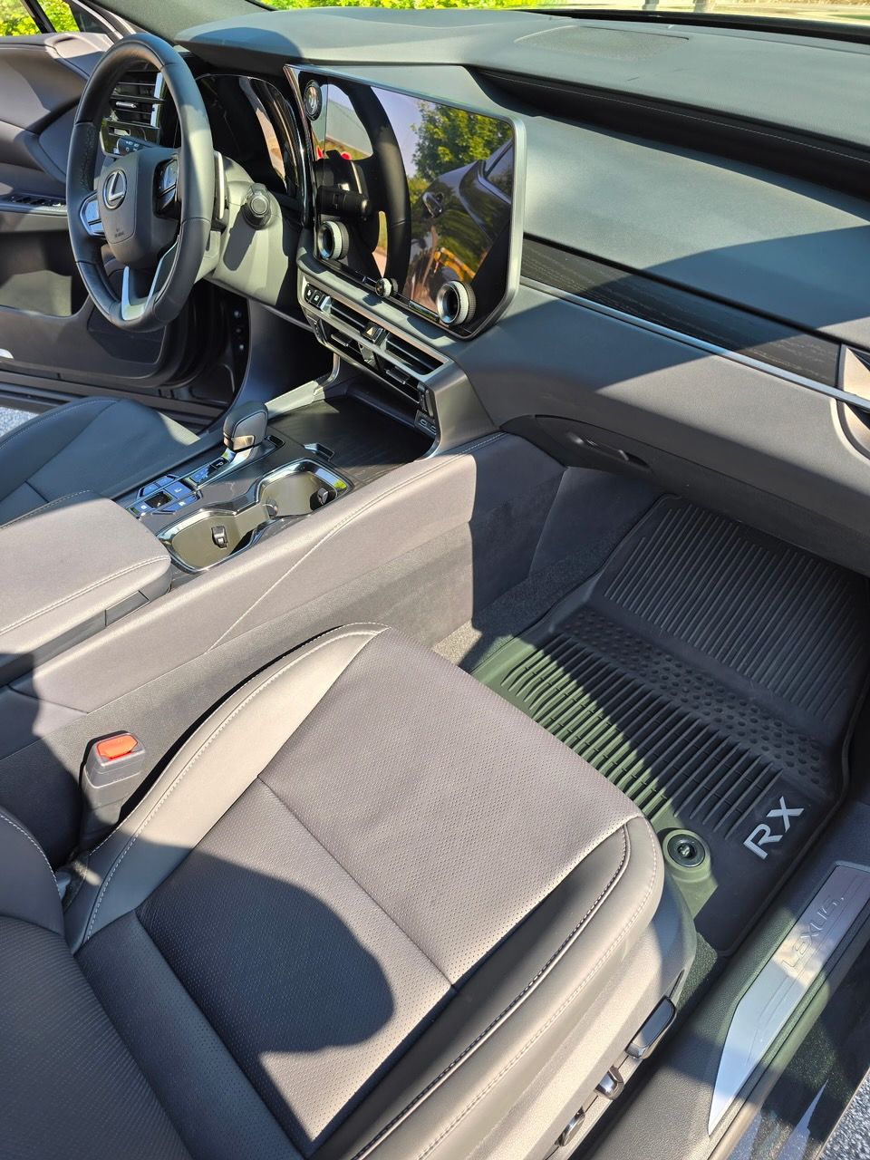 Interior view of a modern Lexus RX driver's seat, steering wheel, dashboard, and black floor mats.