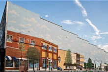 A row of brick downtown storefronts featuring a large sky mural that extends above the roofline.