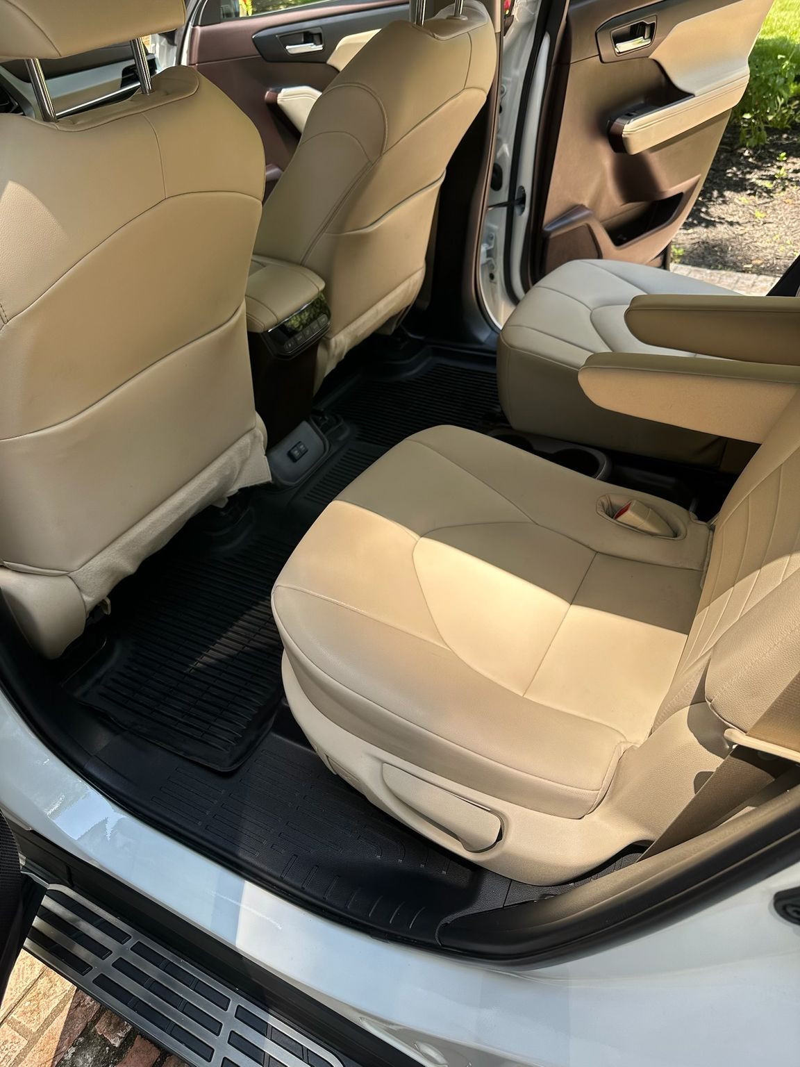 Interior view of a vehicle showing beige leather seats and black floor mats.