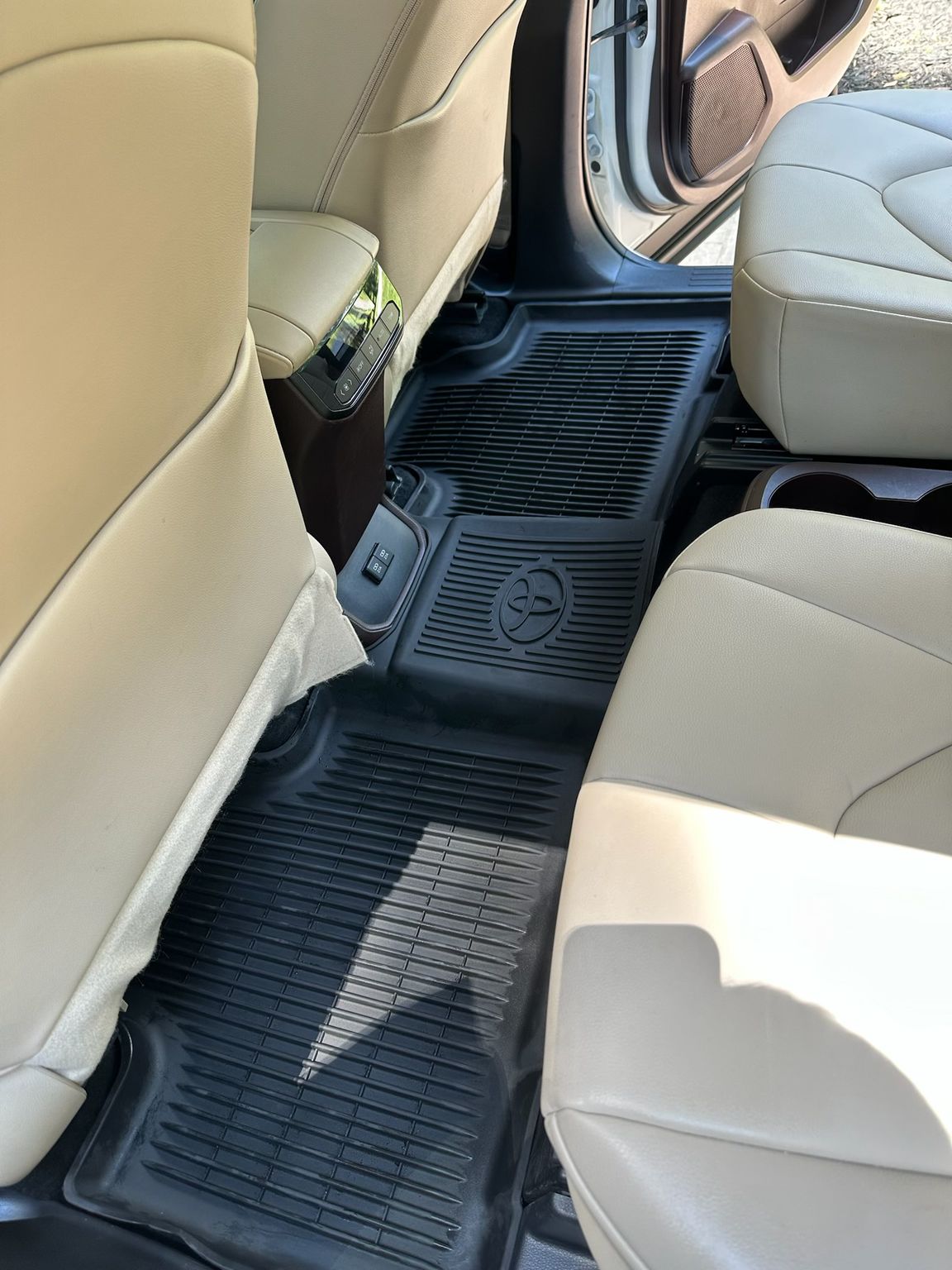 The back seat area of a vehicle with tan upholstery and black rubber floor mats, one featuring a Toyota logo.